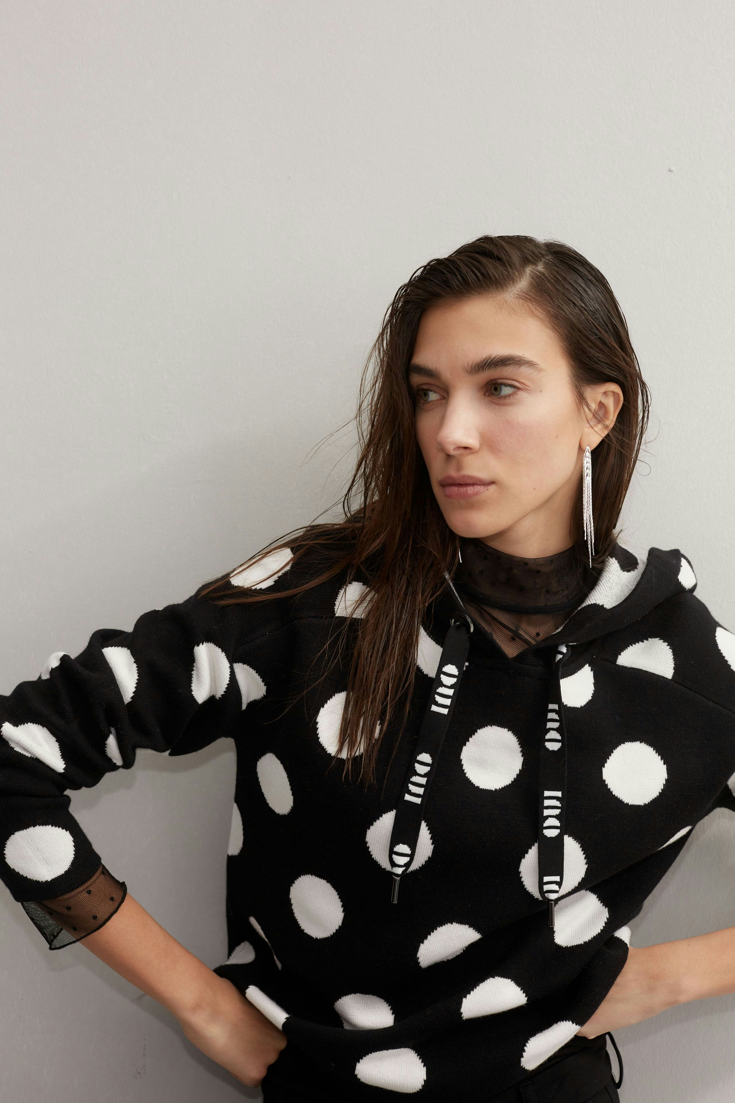 Stylish women's pullover: A woman in a black hoodie with white polka dots poses confidently.