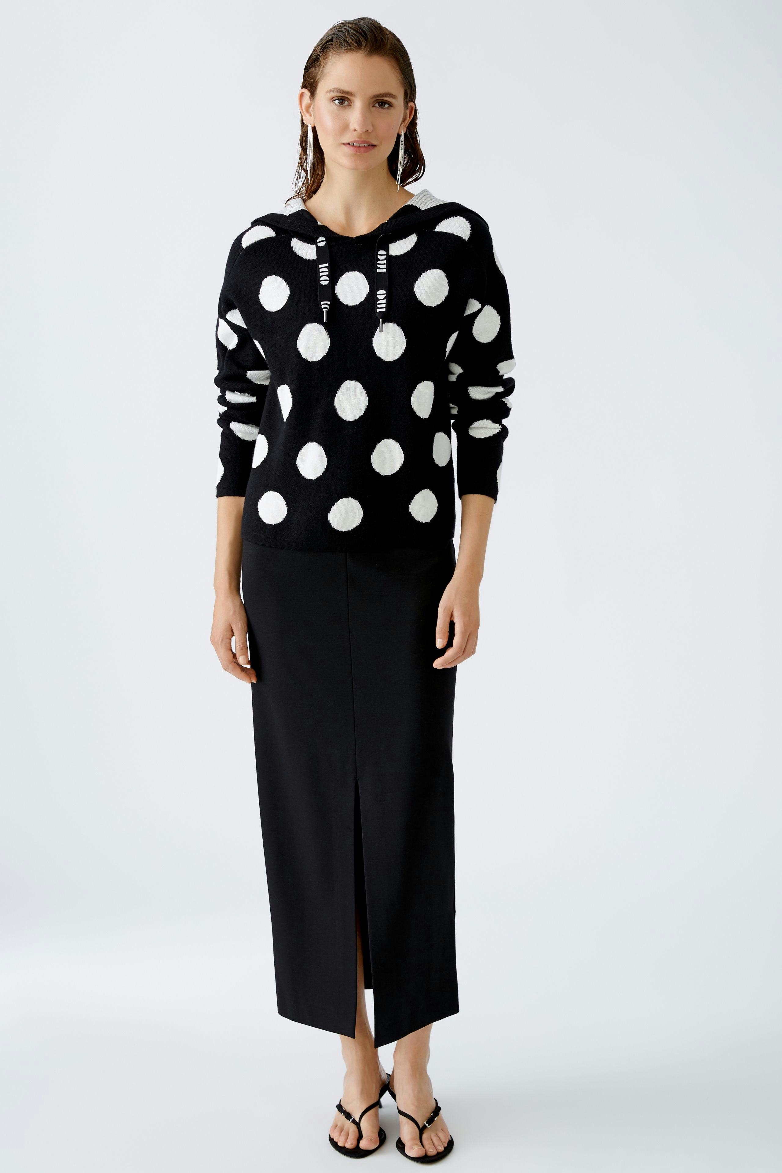 Modern women's pullover: A woman in a black hoodie with white polka dots stands confidently.