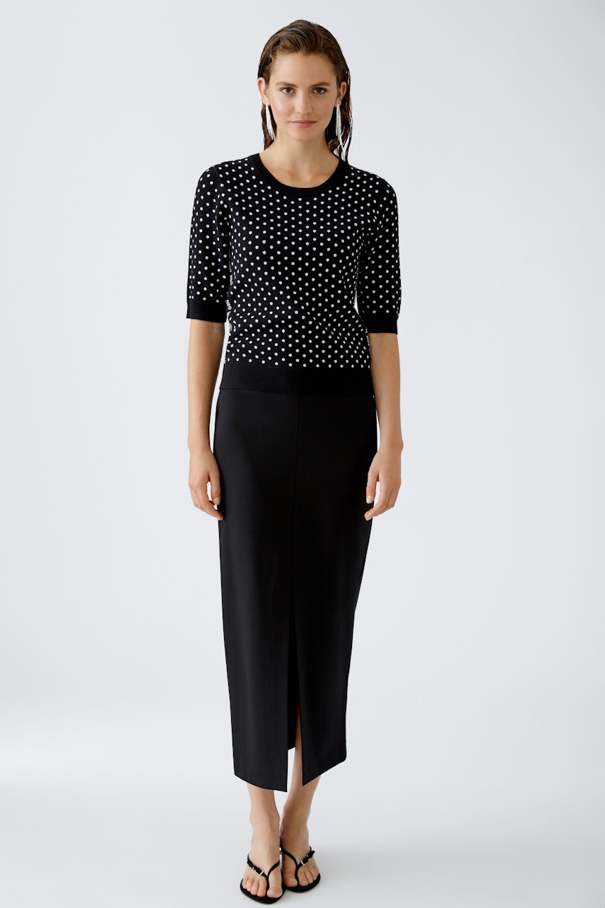 Modern women's pullover: A woman in a black polka dot pullover paired with a sleek skirt.