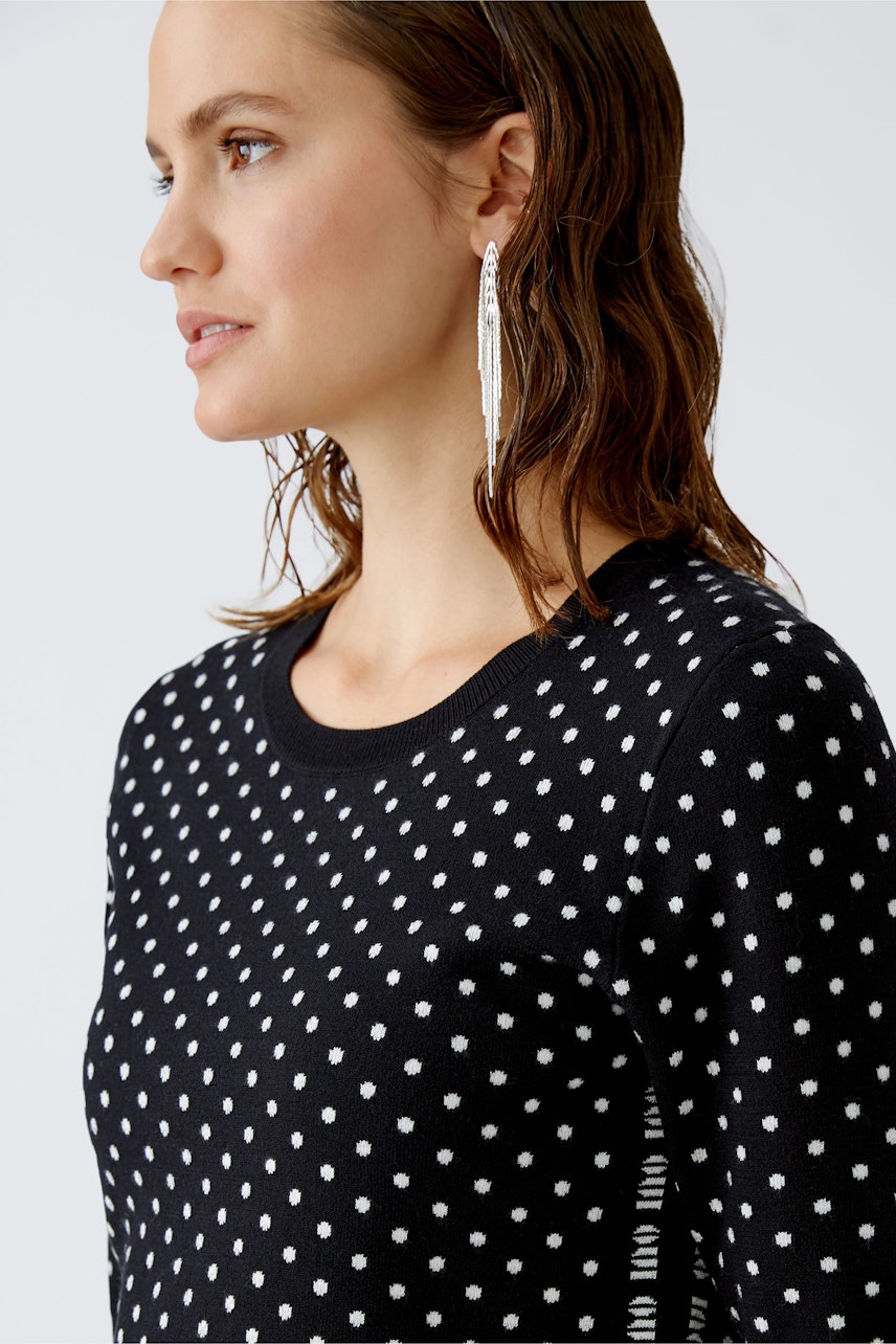 Modern women's pullover: Woman in a black polka dot pullover, showcasing a stylish and casual look.