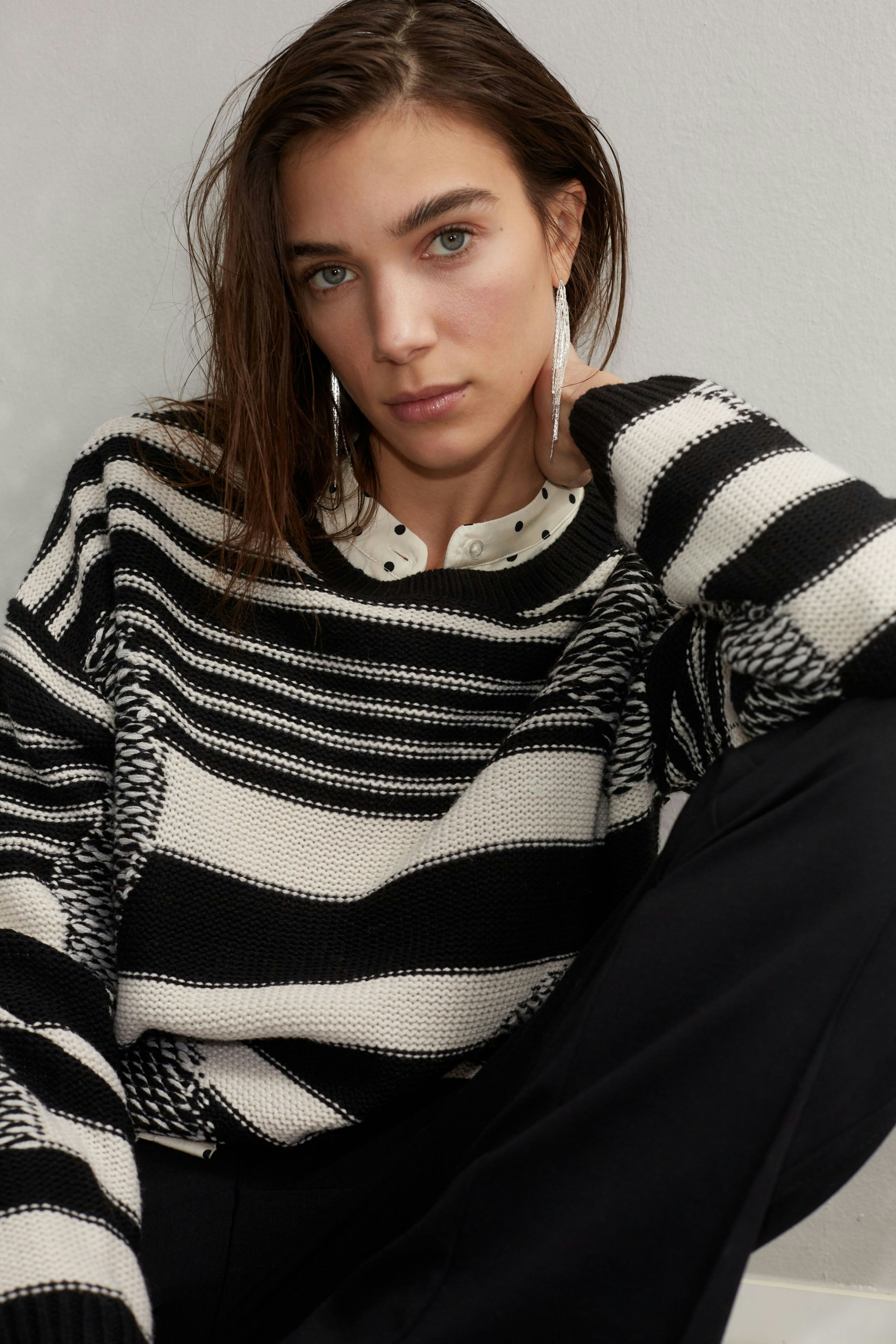 Damen-Pullover: Frau in gestreiftem Pullover in Schwarz und Weiß sitzt entspannt und schaut direkt in die Kamera.