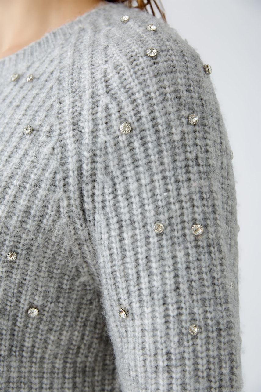 Stylish women's pullover: Close-up of a woman in a grey knitted pullover adorned with sparkling details.