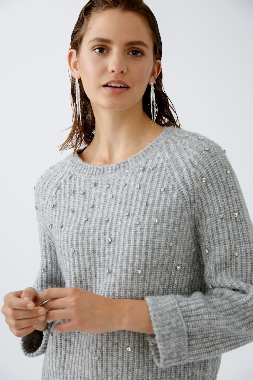 Stylish women's pullover: A woman in a grey ribbed pullover with embellishments looks confidently at the camera.