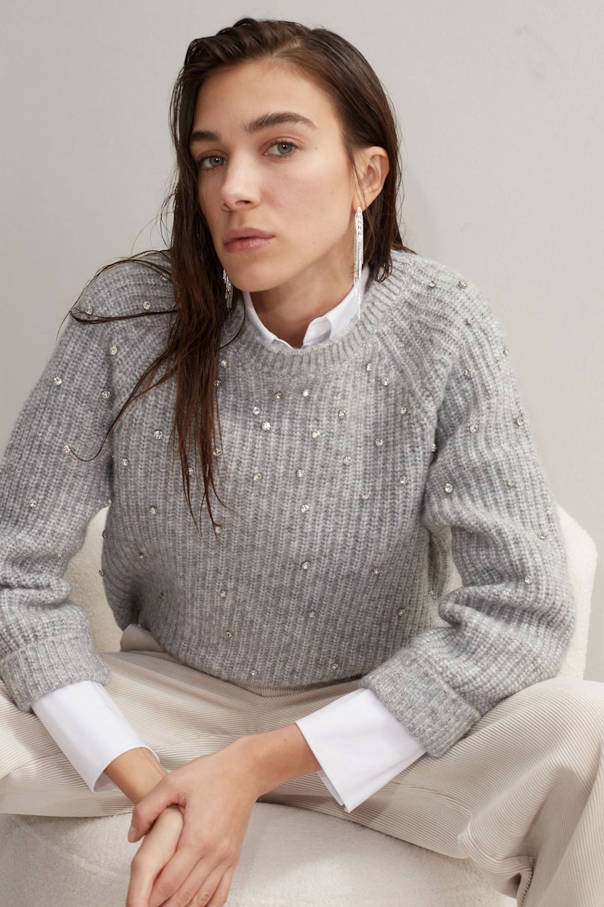 Stylish women's pullover: A woman in a grey pullover with embellishments poses elegantly.