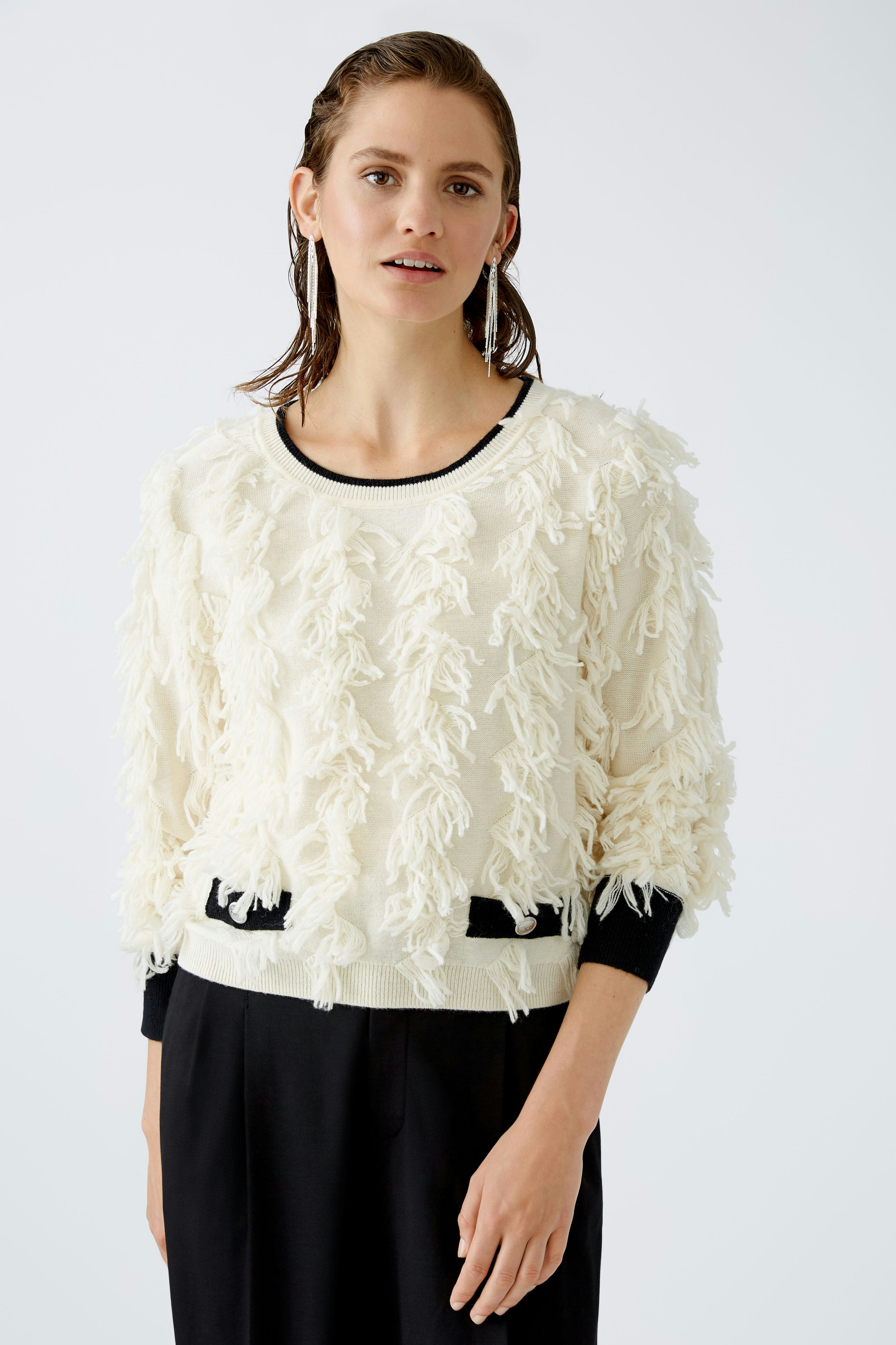 Modern women's pullover: A woman in a fluffy cream pullover with black accents poses confidently.