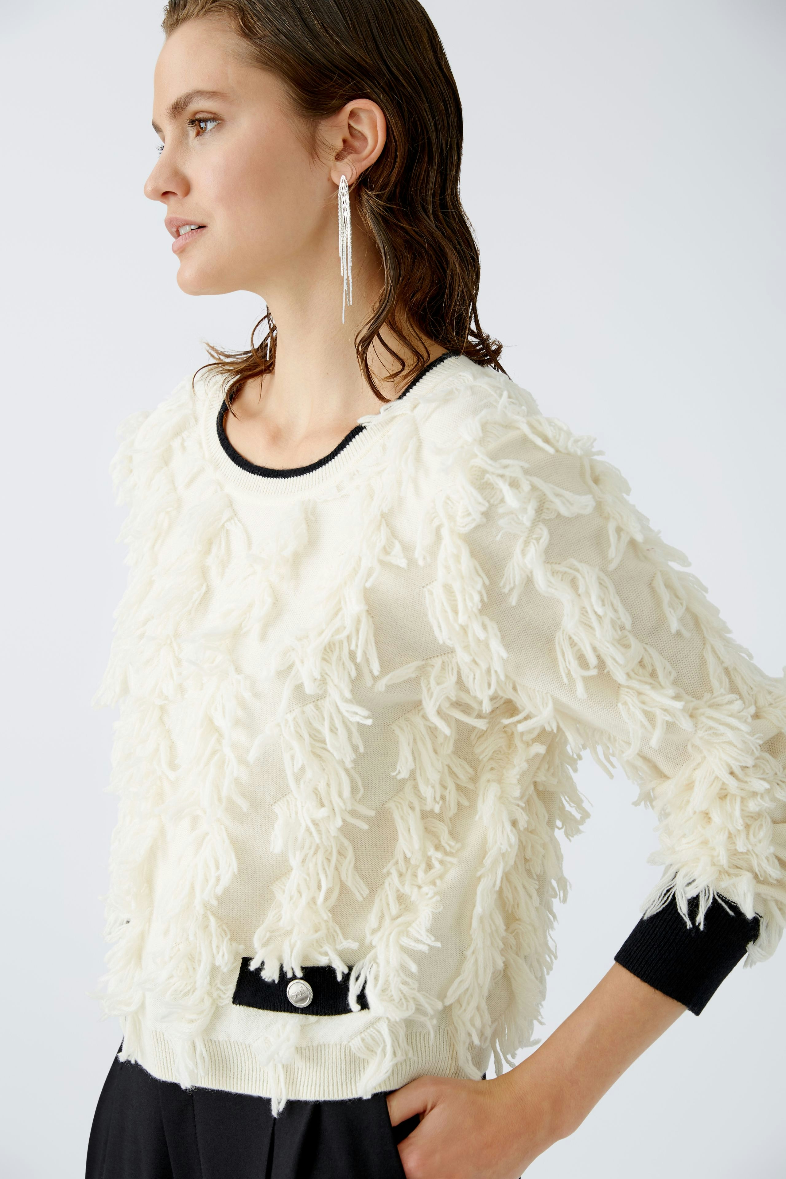 Modern pullover: Woman in a textured cream pullover with fringes, styled effortlessly.