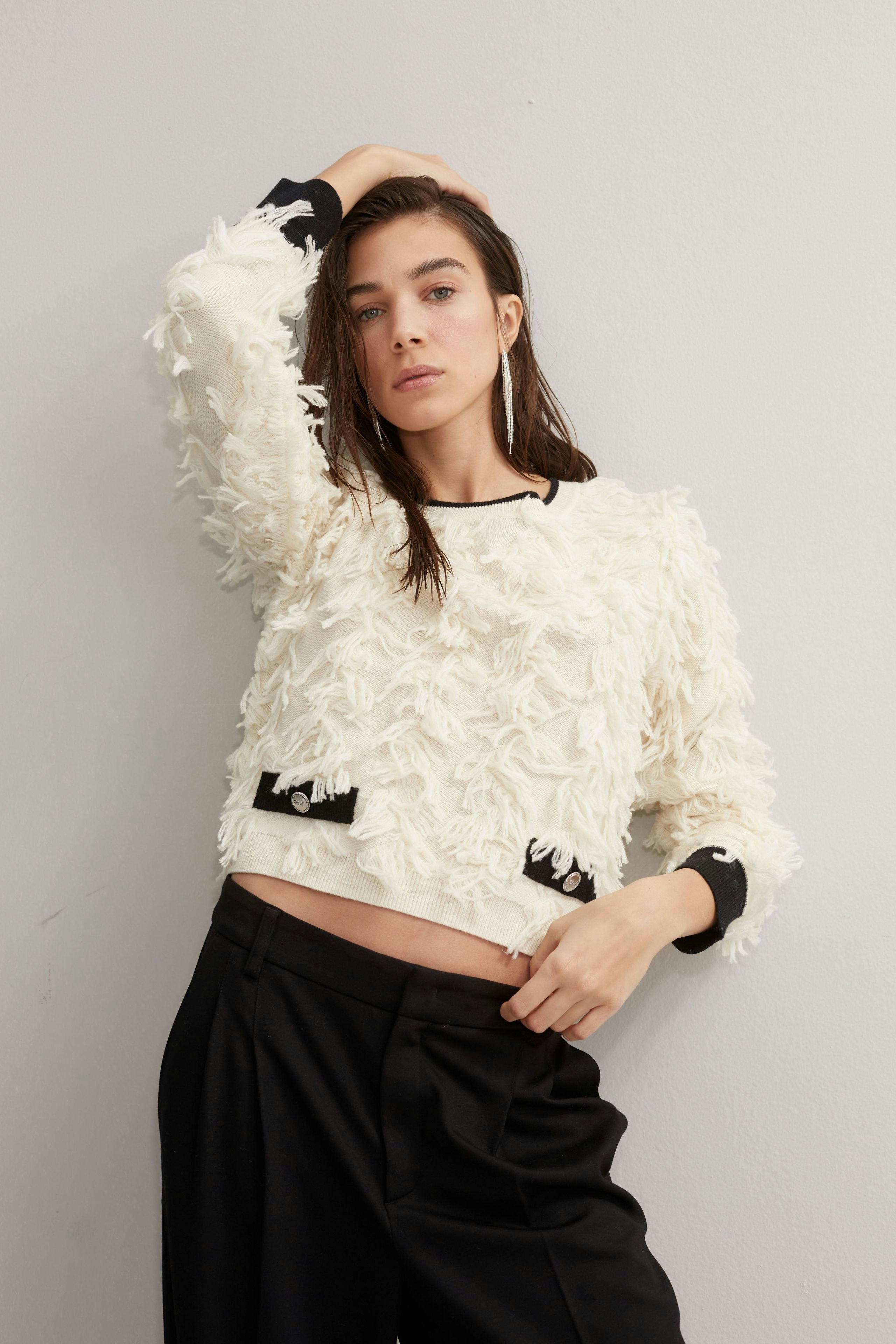 Modern women's pullover: A woman in a textured cream pullover with black accents poses confidently.