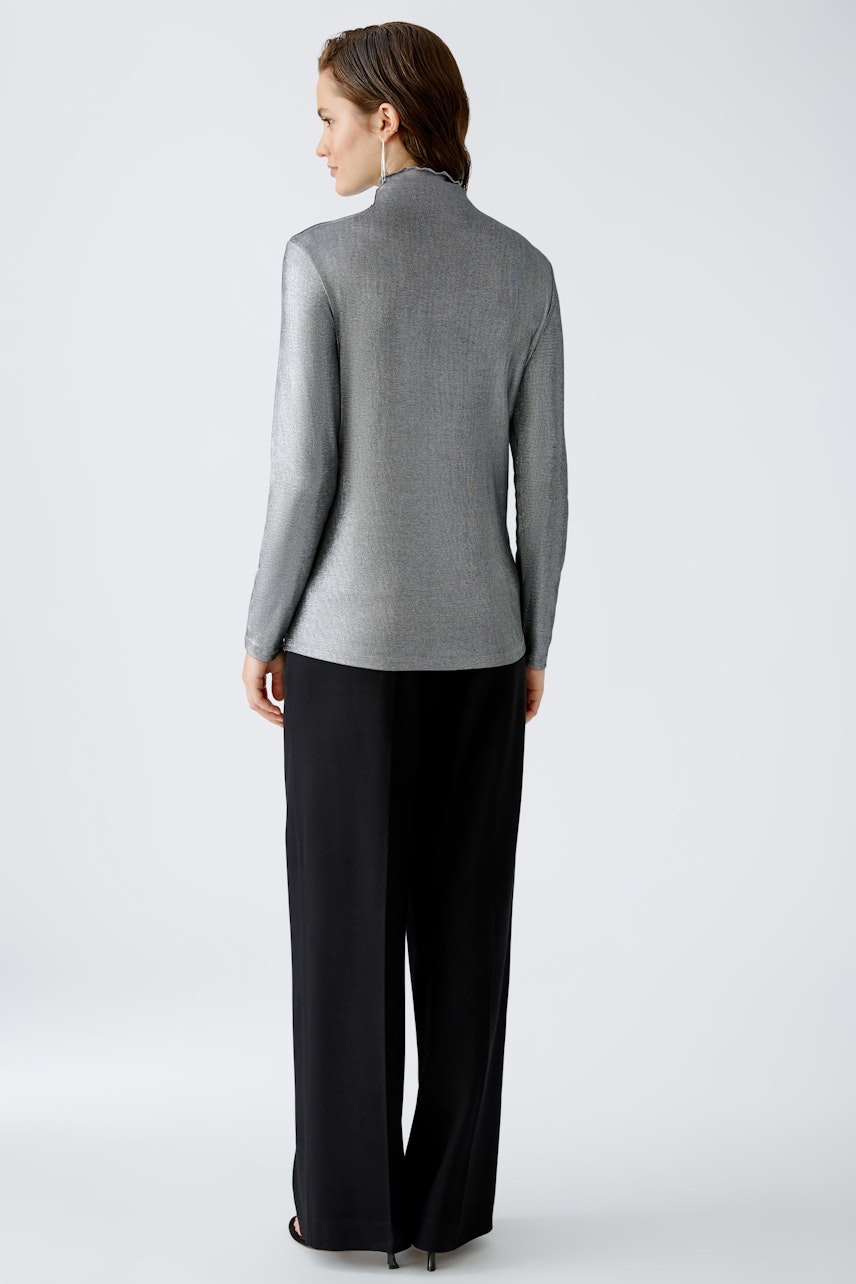 Stylish long-sleeve shirt: Woman in a sleek silver pullover paired with elegant black trousers.