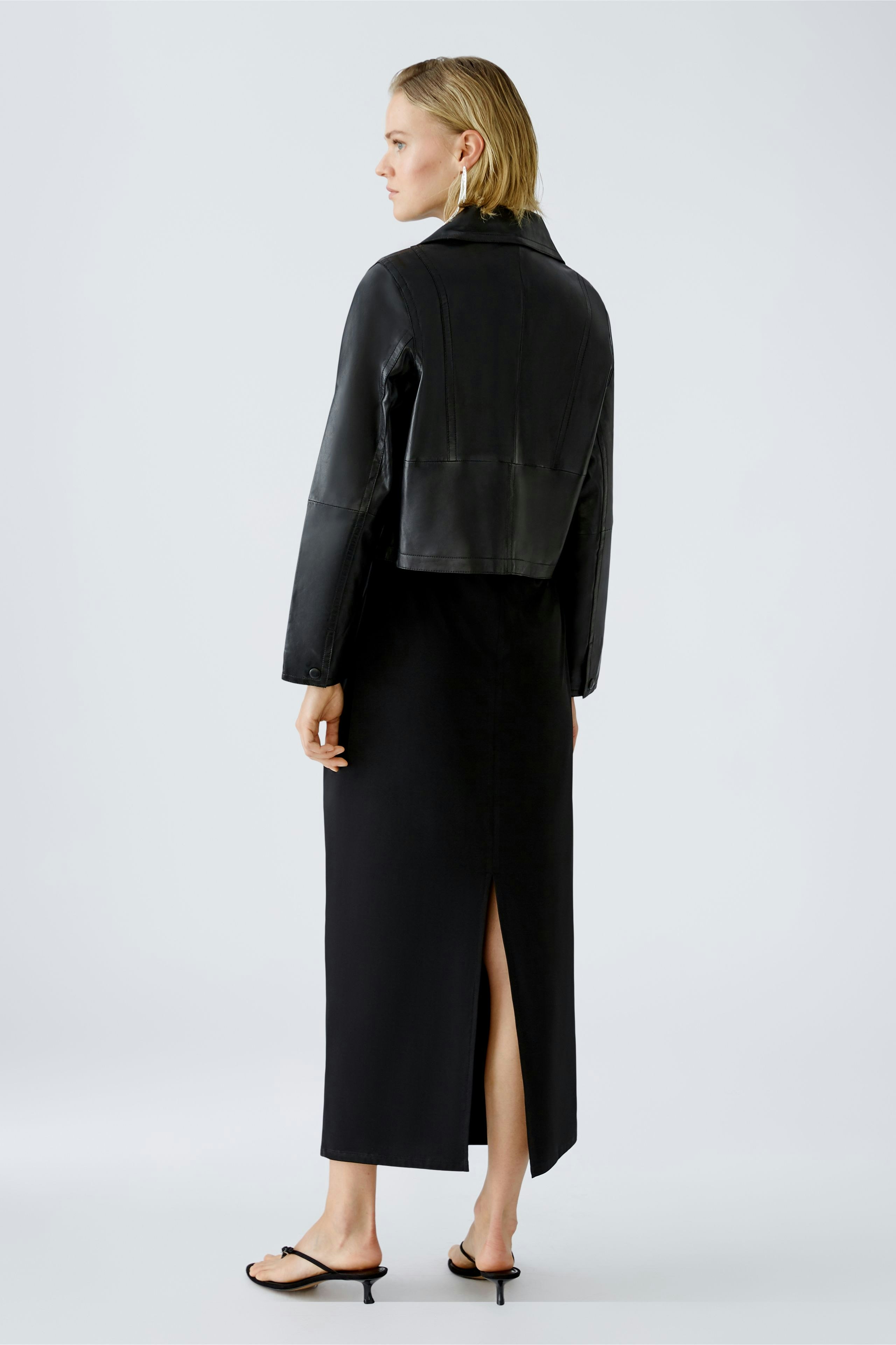 Stylish biker jacket: Woman in a cropped black leather jacket paired with a sleek black dress.