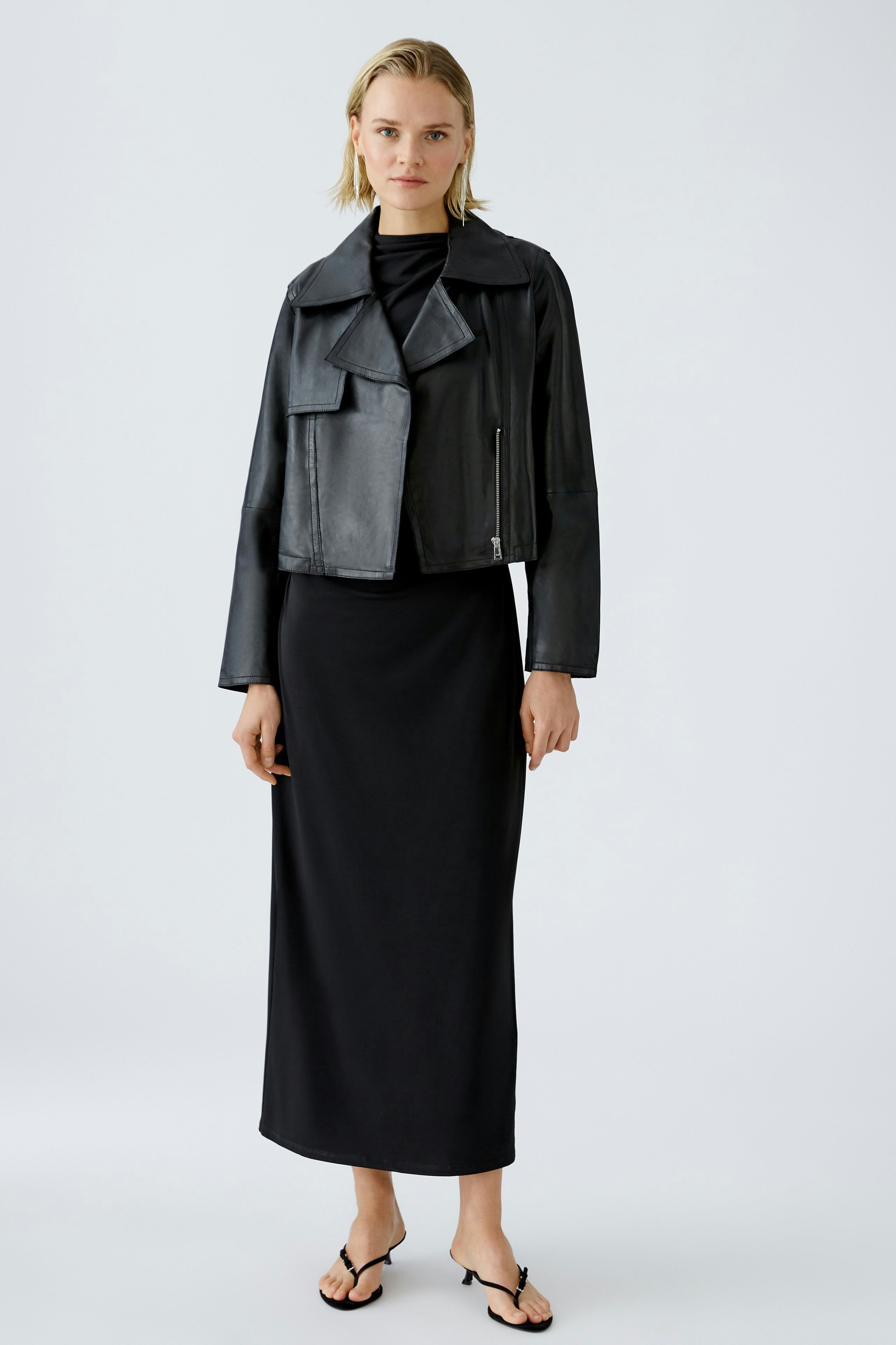 Stylish biker jacket: Confident woman in a black leather biker jacket over a sleek dress.