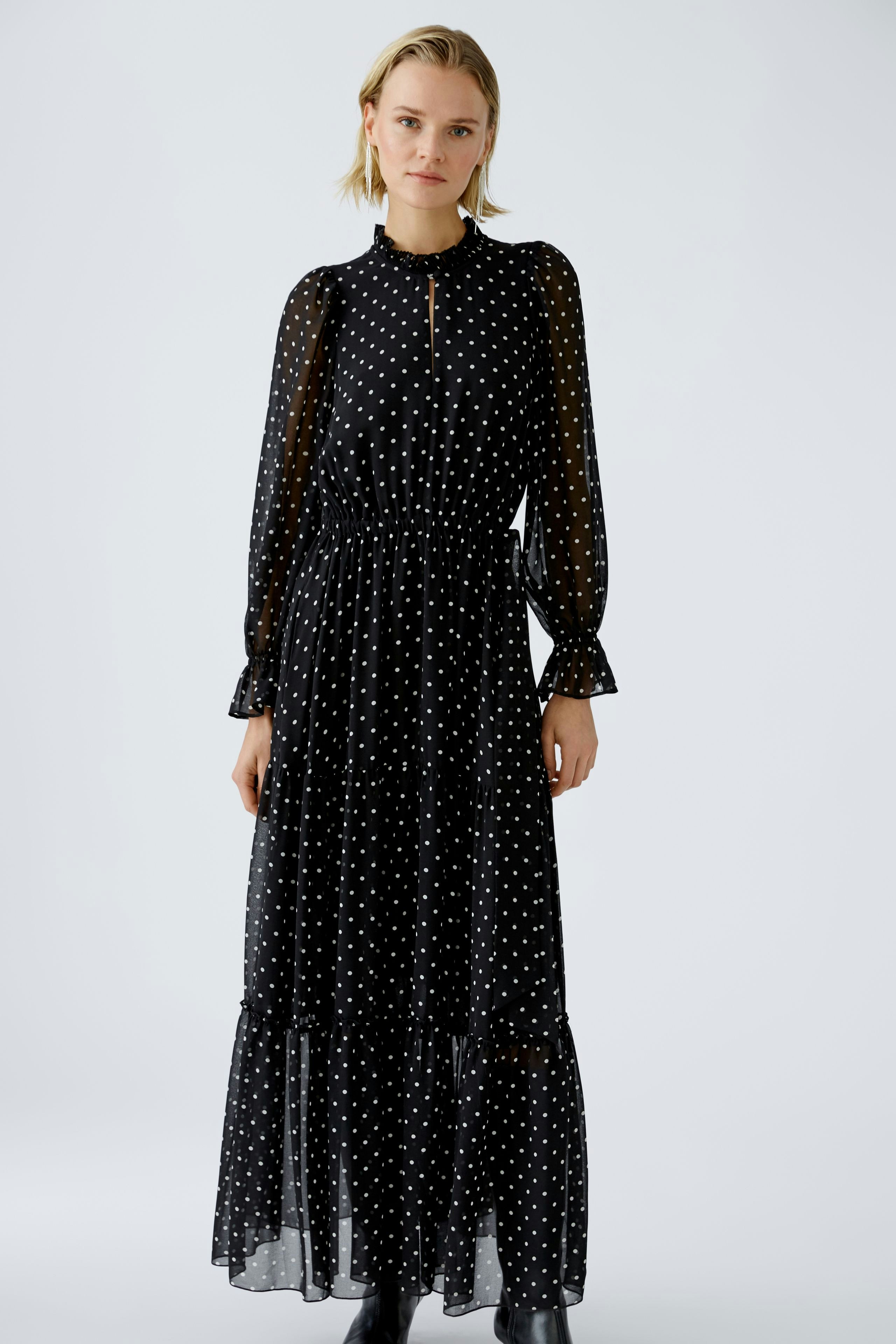 Elegant evening dress: A woman in a black polka dot maxi dress with a high neck and flowing sleeves.