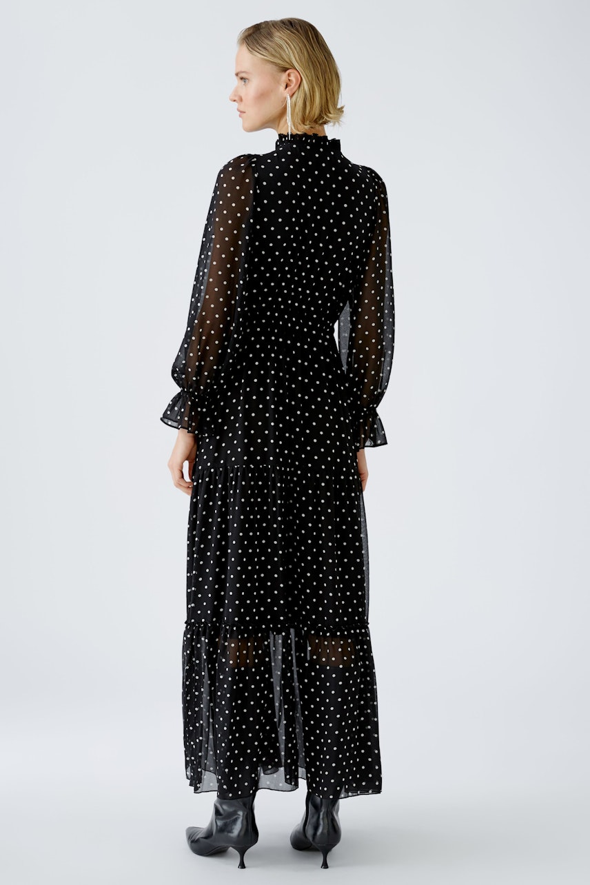 Elegant evening dress: Woman in a black polka dot dress with long sleeves and a flowing silhouette.