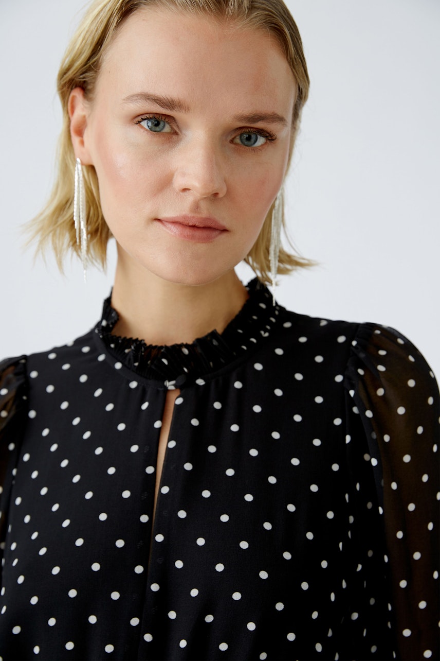 Elegant evening dress: Woman in a black polka dot dress with a ruffled collar, exuding sophistication.