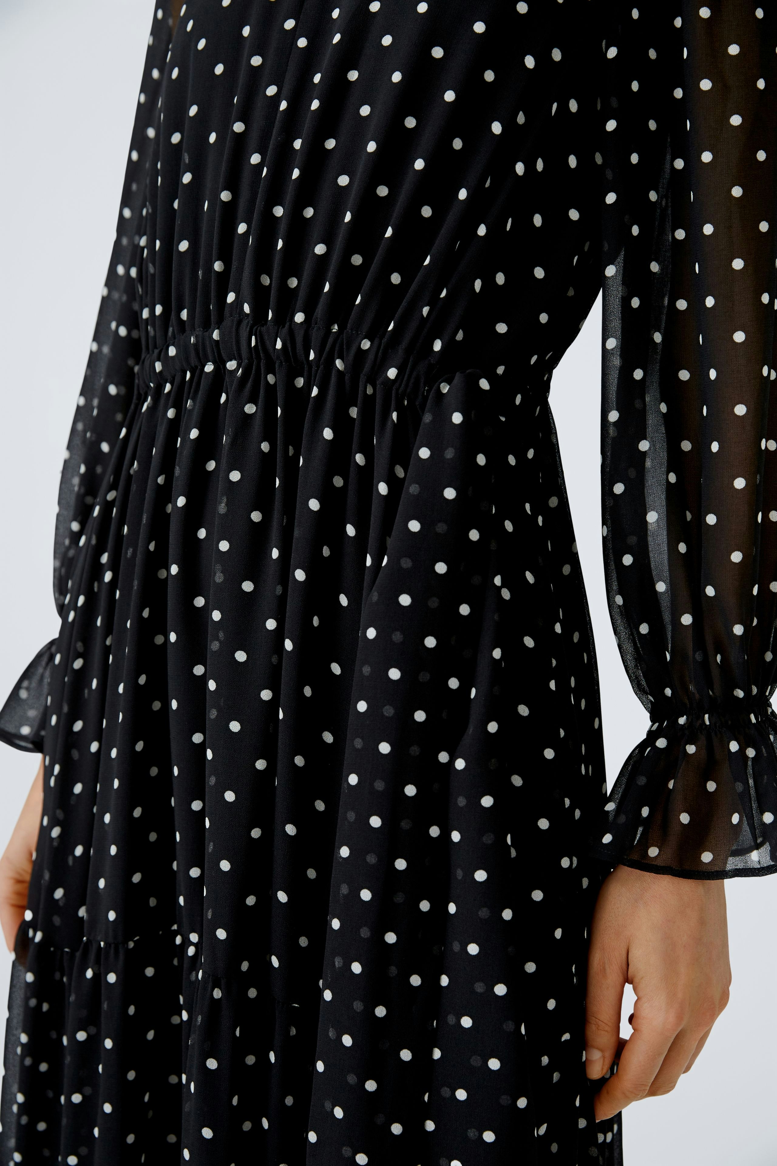 Elegant evening dress: A woman in a black polka dot dress with flowing sleeves, showcasing timeless style.