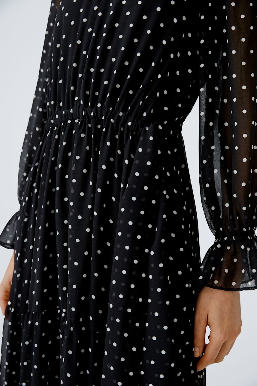 Elegant evening dress: A woman in a black polka dot dress with flowing sleeves, showcasing timeless style.