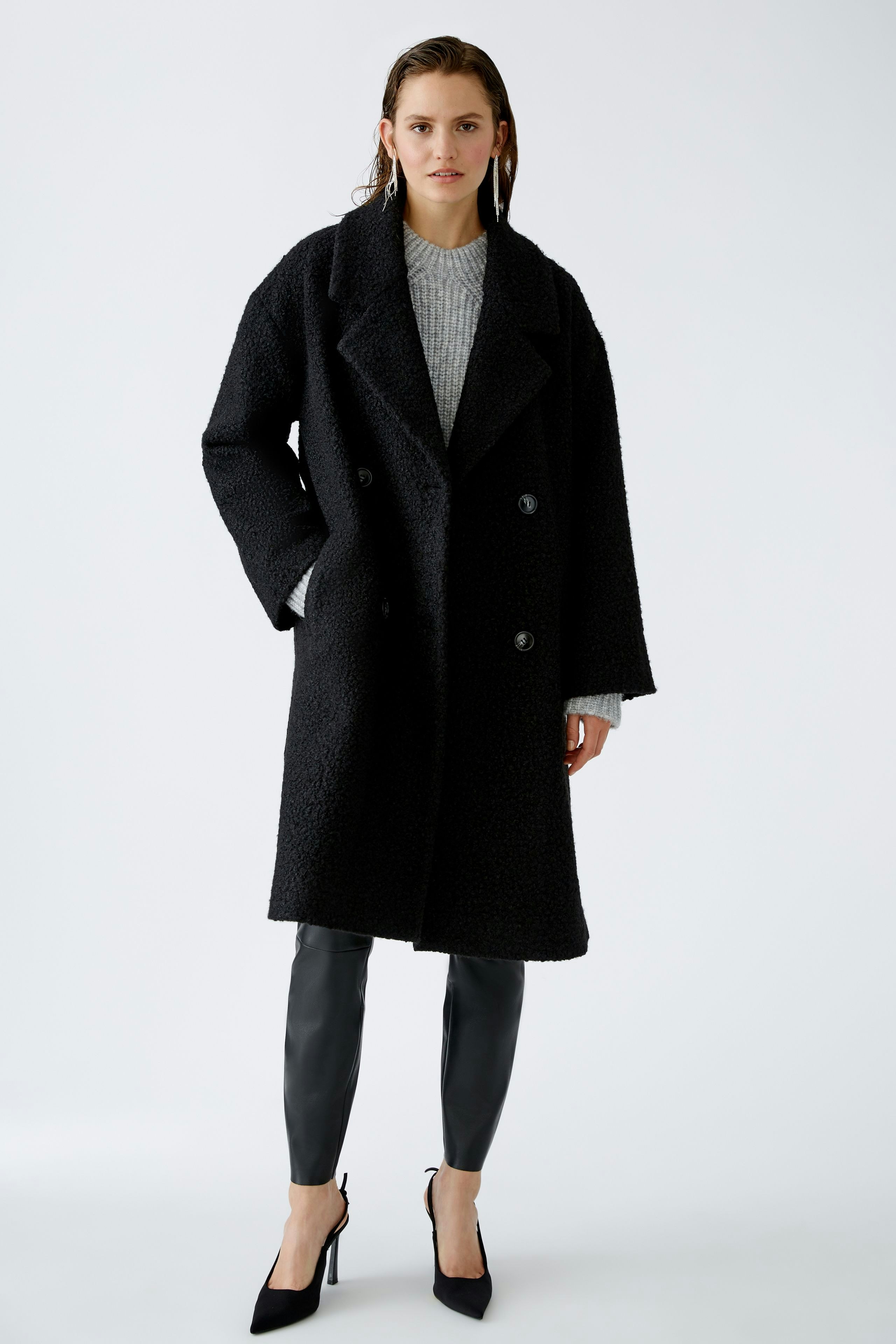 Stylish winter coat: A woman in a black oversized coat over a gray pullover, exuding elegance.