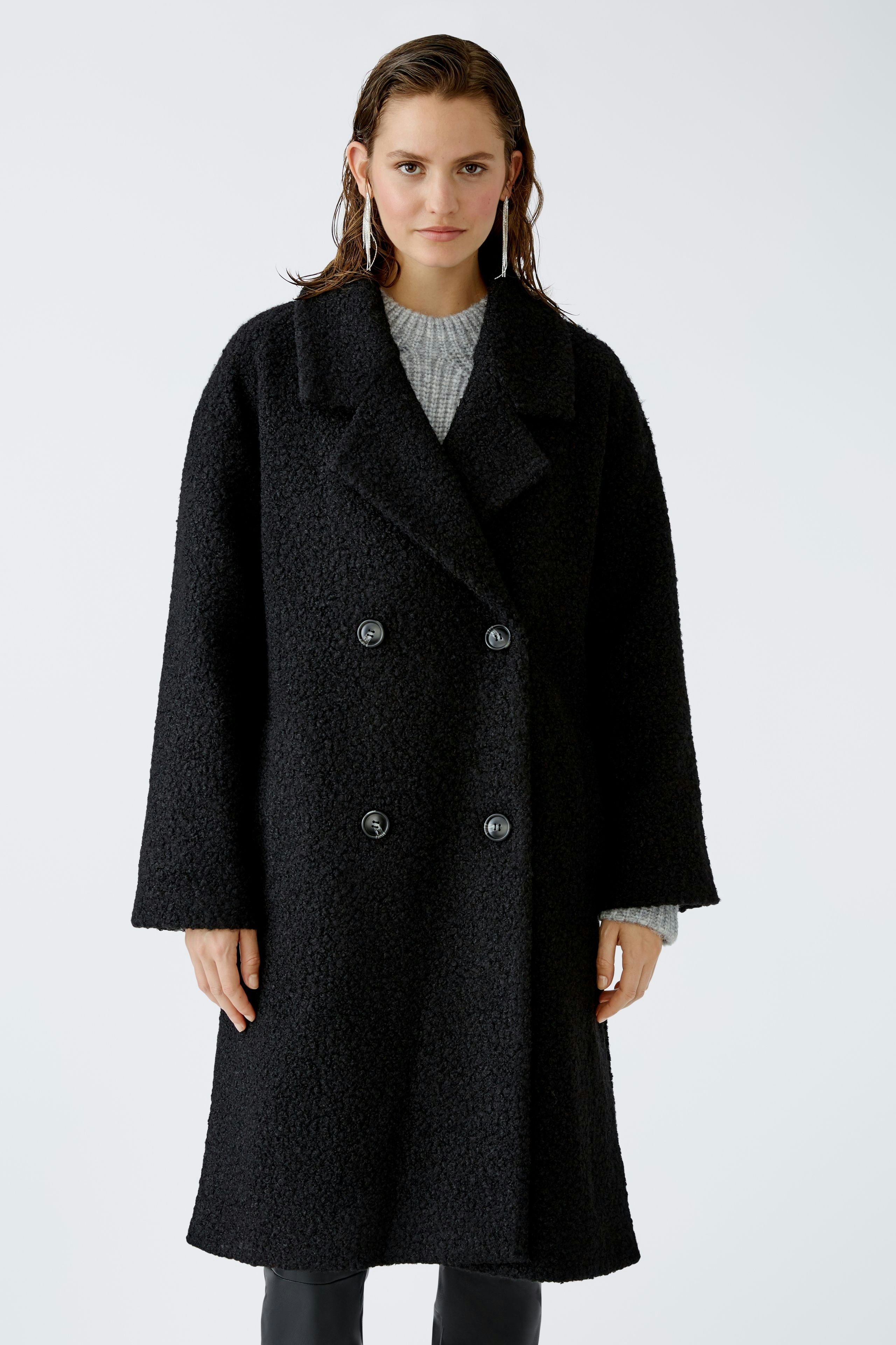 Stylish winter coat: A woman in a black double-breasted coat stands confidently against a plain background.