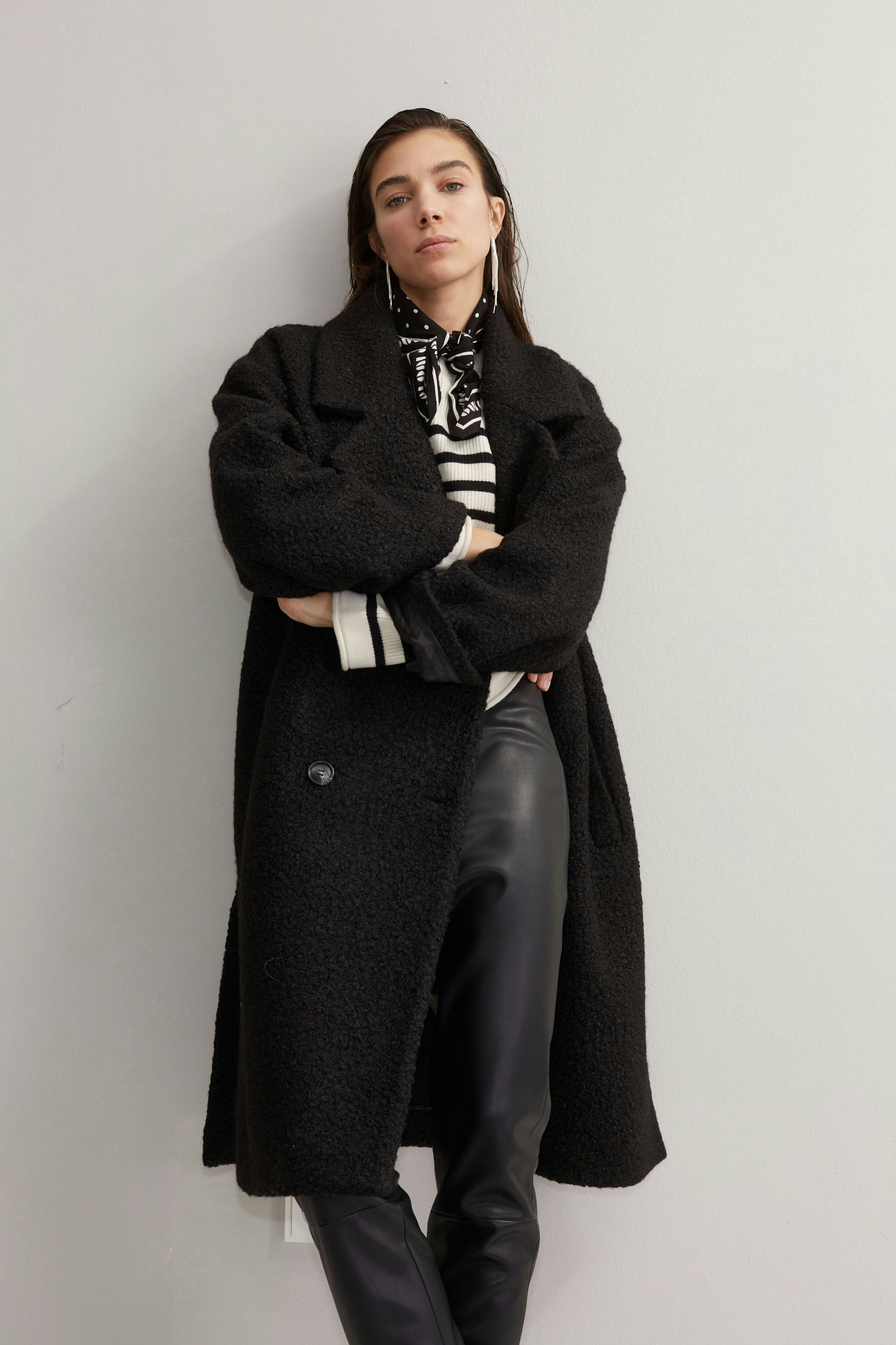 Stylish women's winter coat: A woman in a black coat over a striped shirt poses confidently.