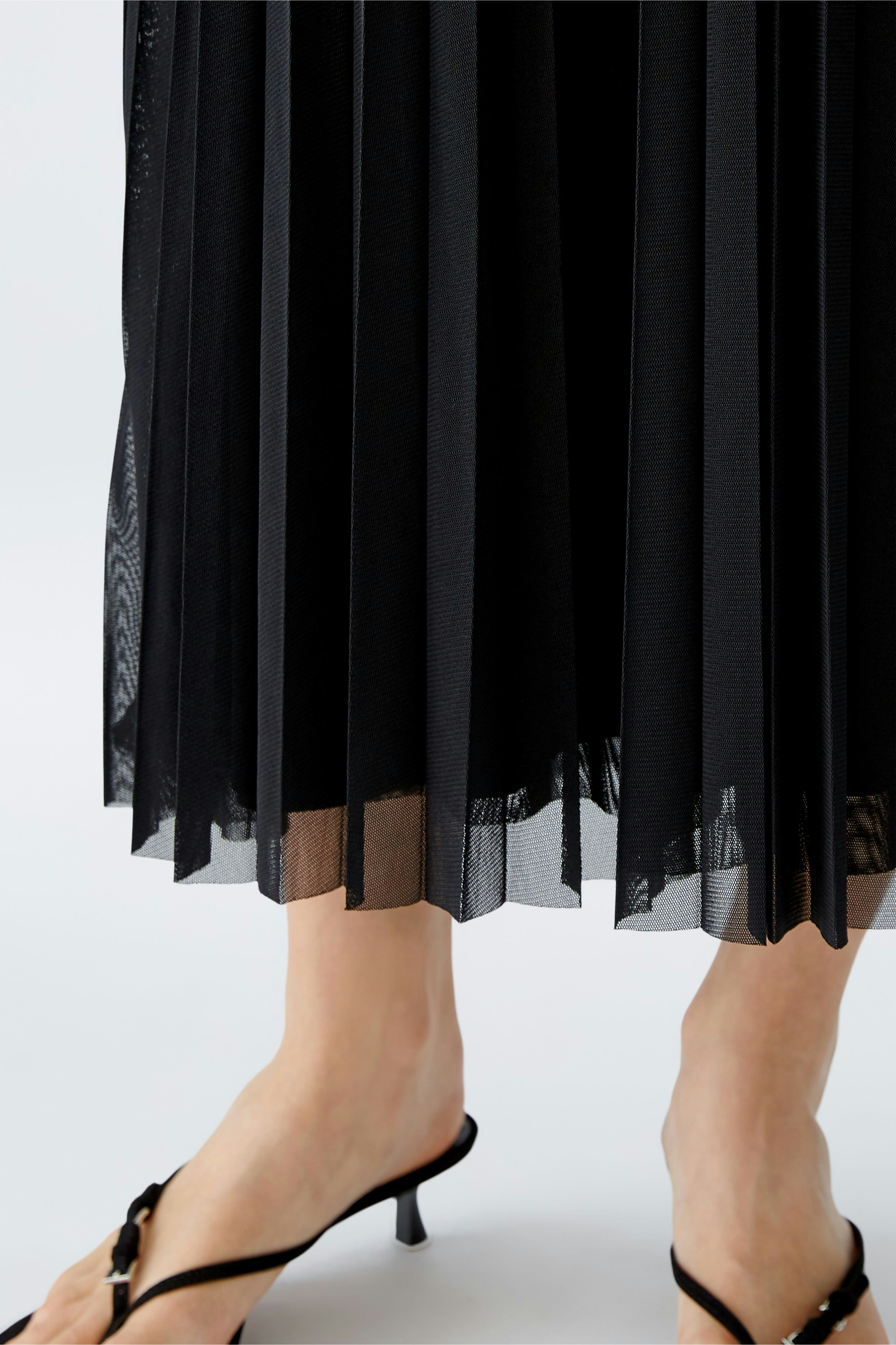 Eleganter Plisseerock: Frau trägt einen schwarzen, schwingenden Rock mit feinen Falten und modischen Sandalen.