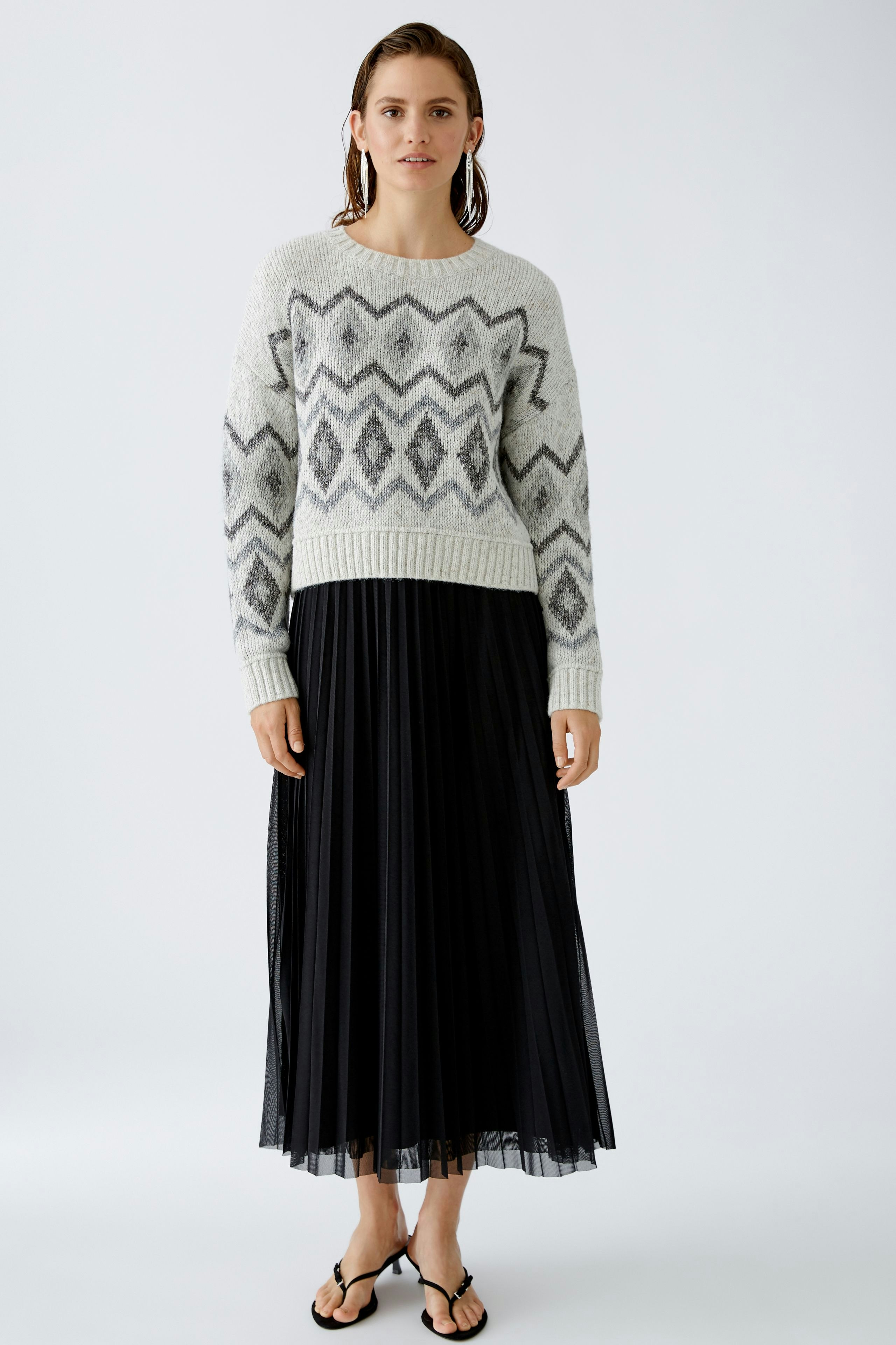 Eleganter Plisseerock: Frau in schwarzem Plisseerock kombiniert mit einem gemusterten Pullover.