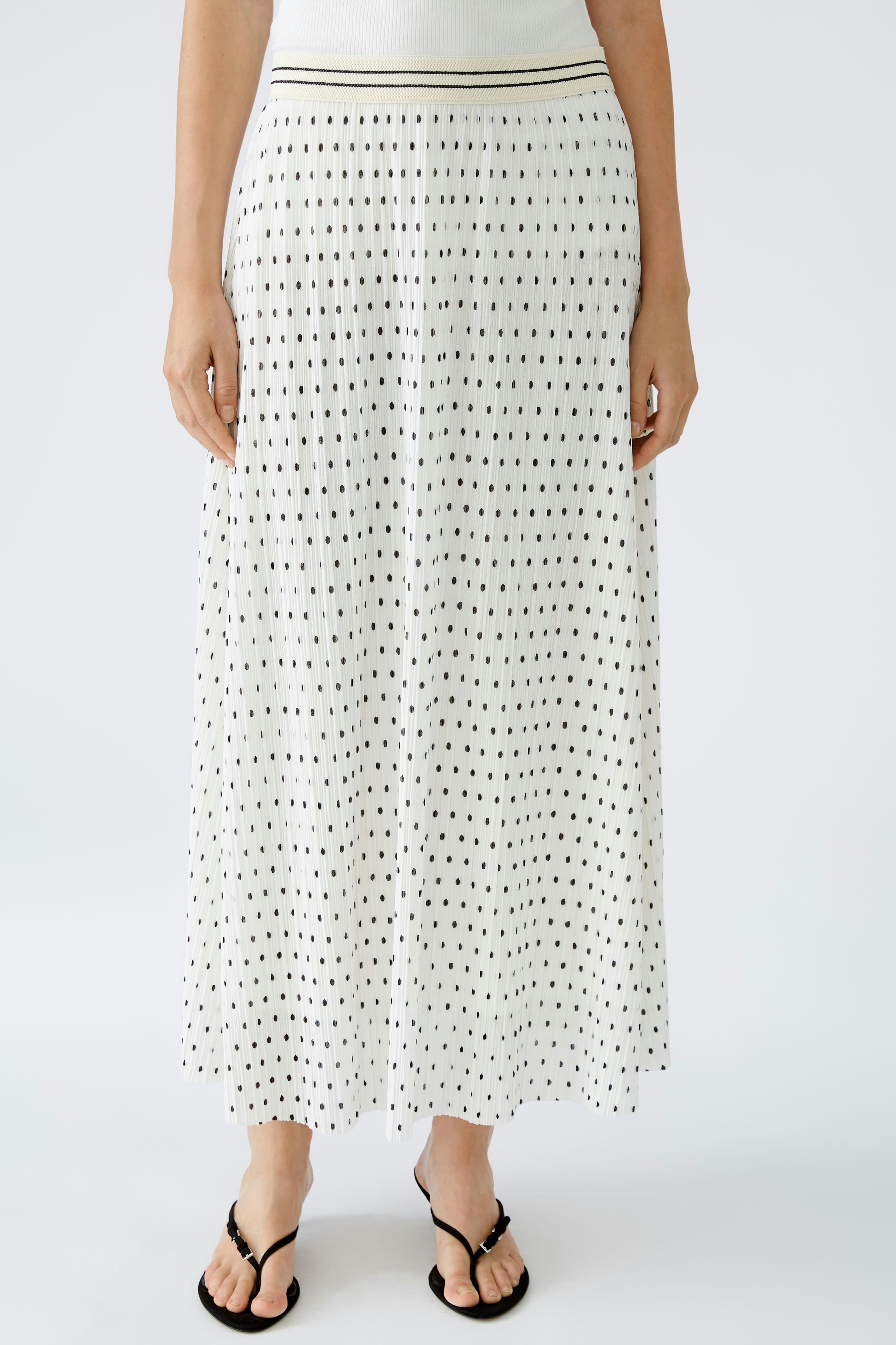 Elegant pleated skirt: Woman in a flowing white skirt with a dotted pattern stands confidently.