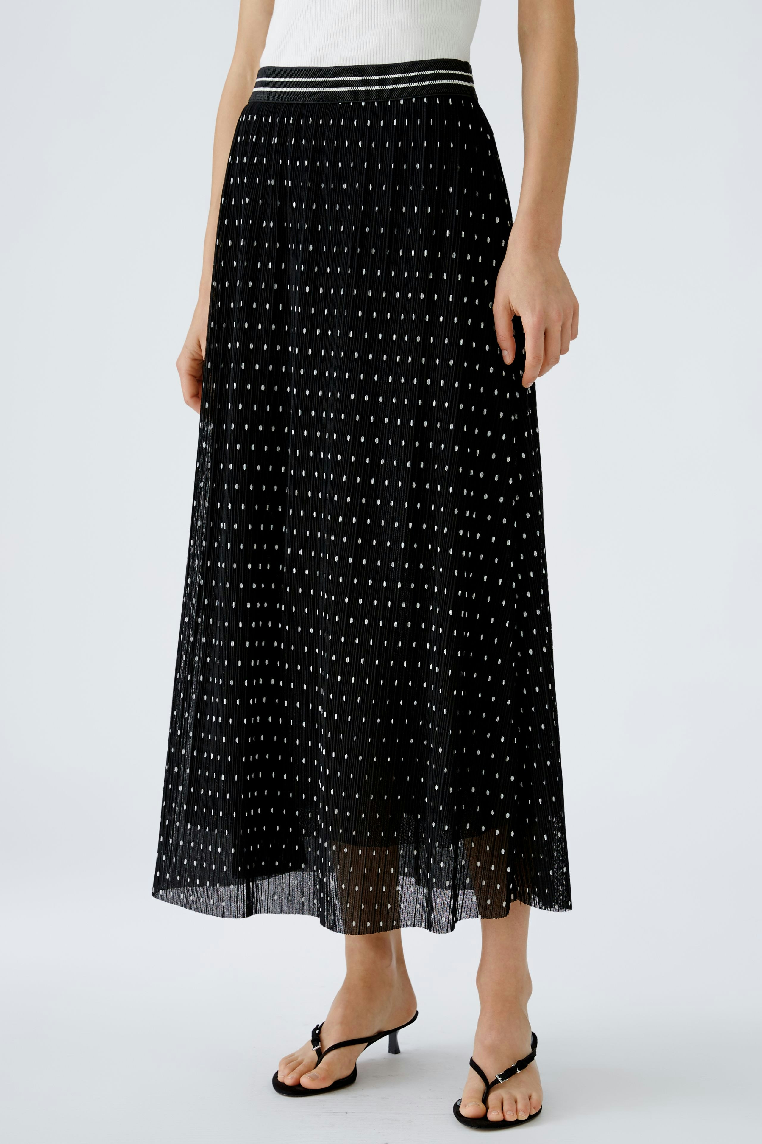 Elegant pleated skirt: Woman in a black pleated skirt with white dots, styled for a chic look.