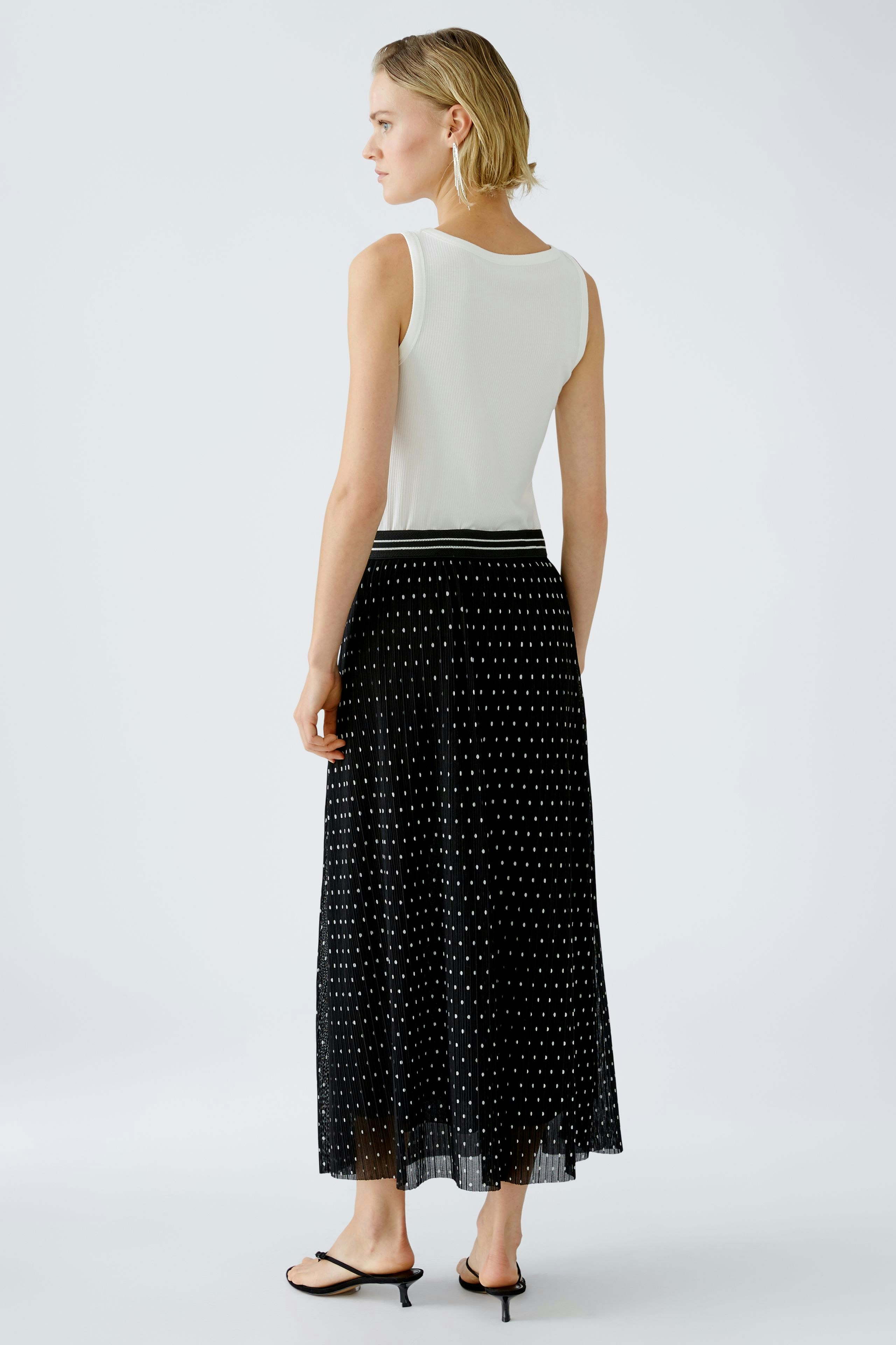 Elegant pleated skirt: Young woman in a stylish black pleated skirt with a white top, showcasing a chic look.