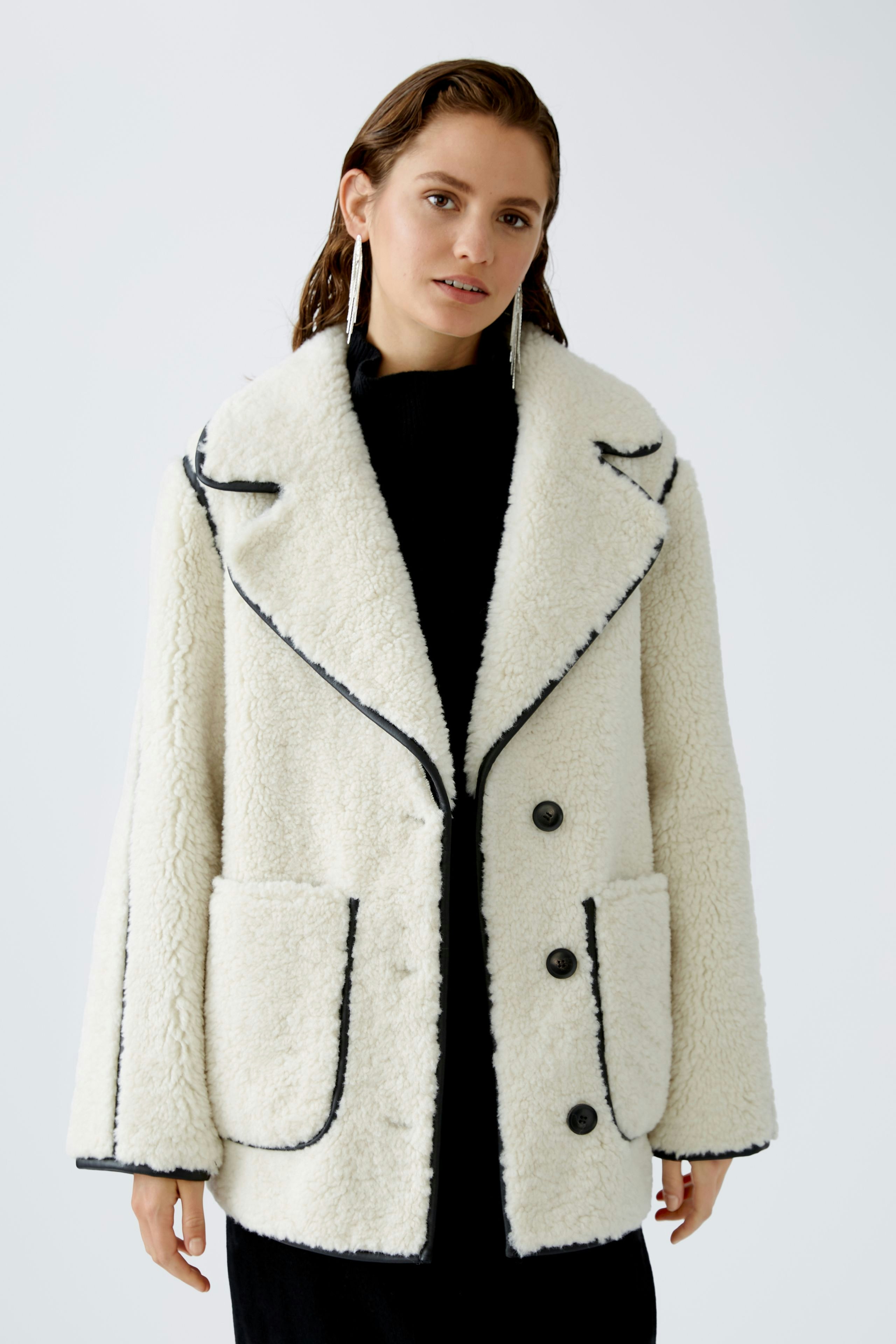 Moderne Outdoorjacke: Frau in einer weißen, kuscheligen Jacke mit großen Taschen und schwarzem Kragen.