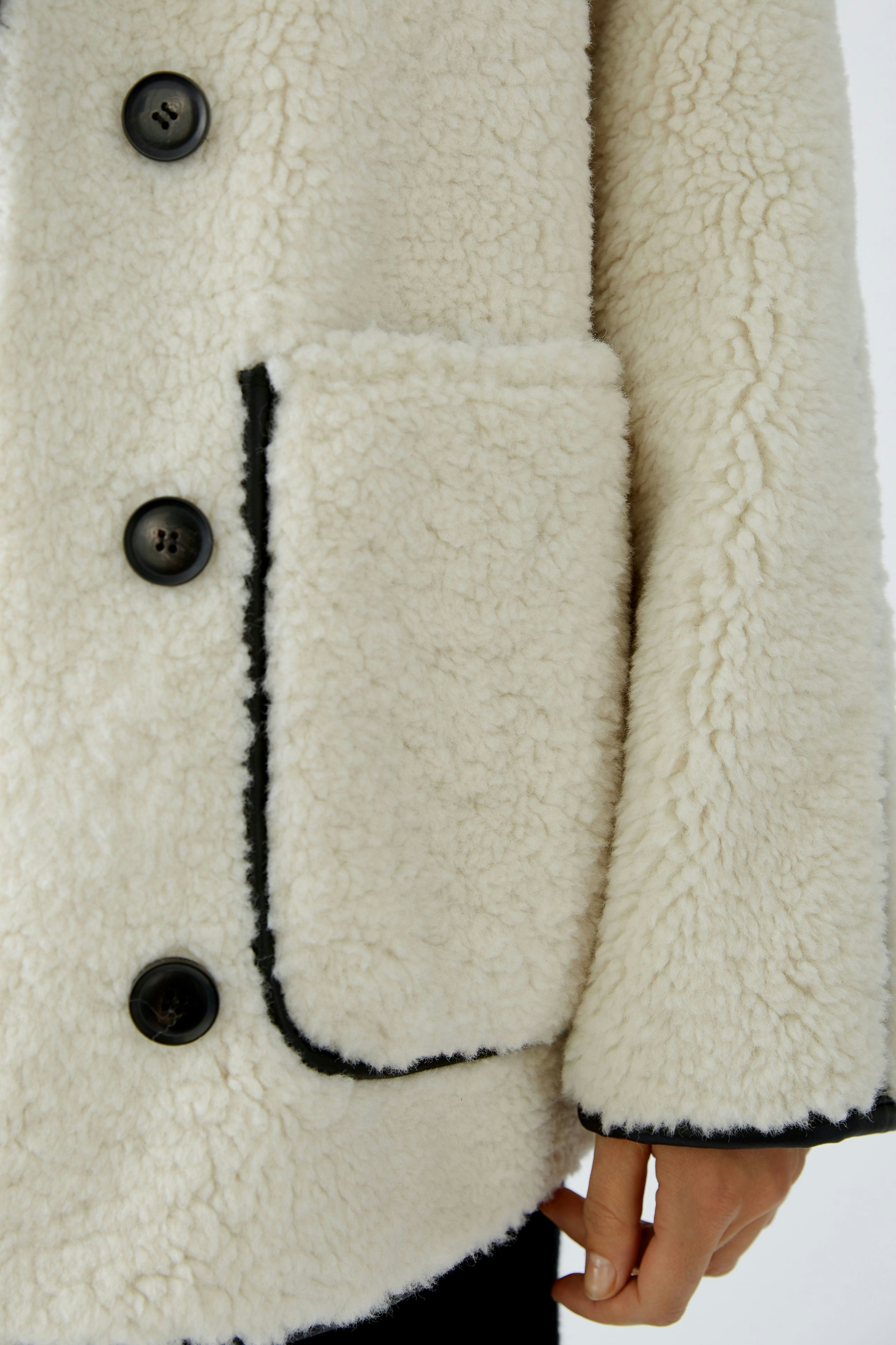 Gemütliche Outdoorjacke: Frau in einer weißen, flauschigen Jacke mit Knöpfen und Taschen.