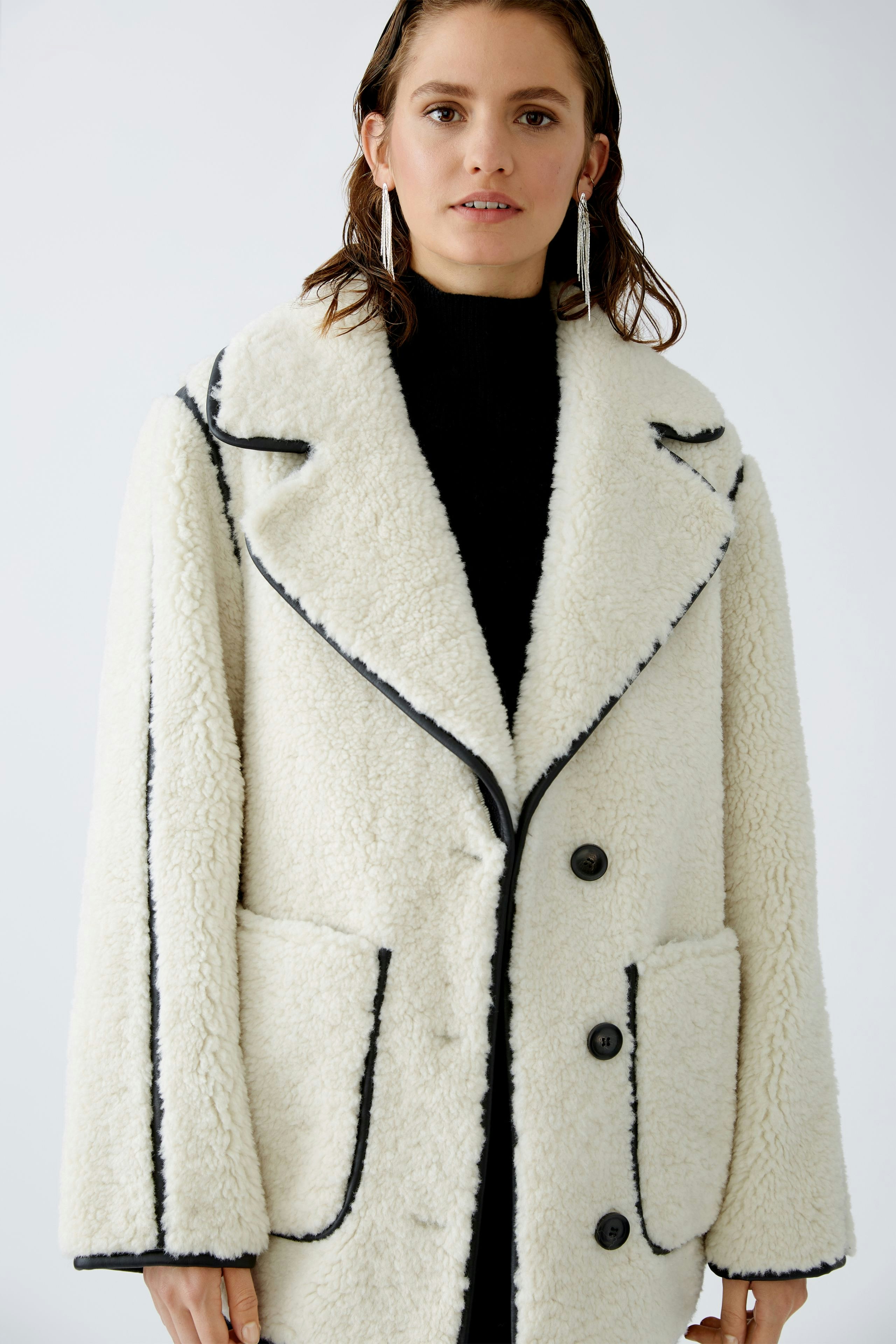 Damen-Outdoojacke: Frau in einer weißen, kuscheligen Jacke mit schwarzen Akzenten und großen Taschen.