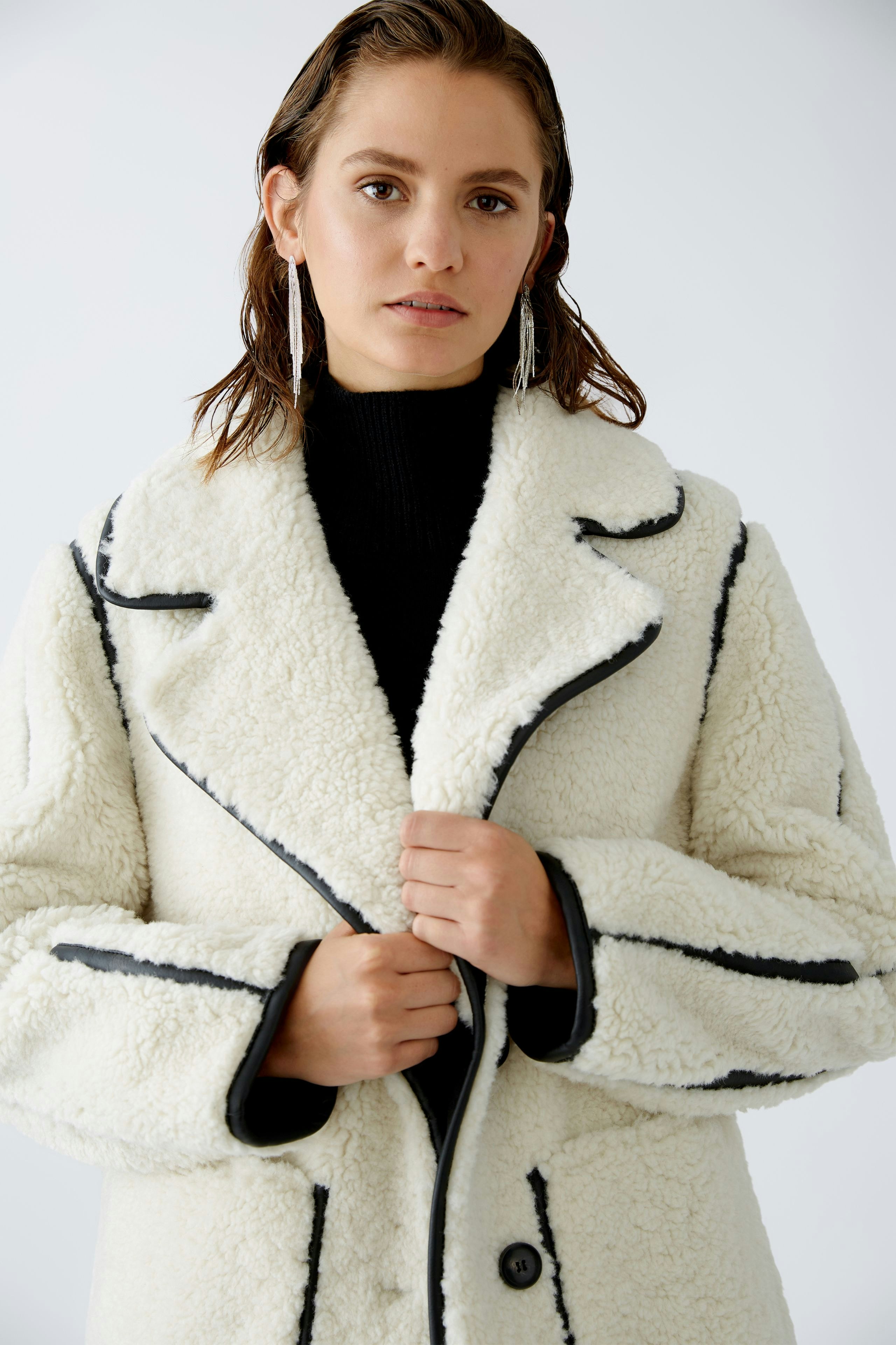 Moderne Outdoorjacke: Frau in einer weißen, kuscheligen Jacke mit schwarzen Akzenten, die selbstbewusst posiert.