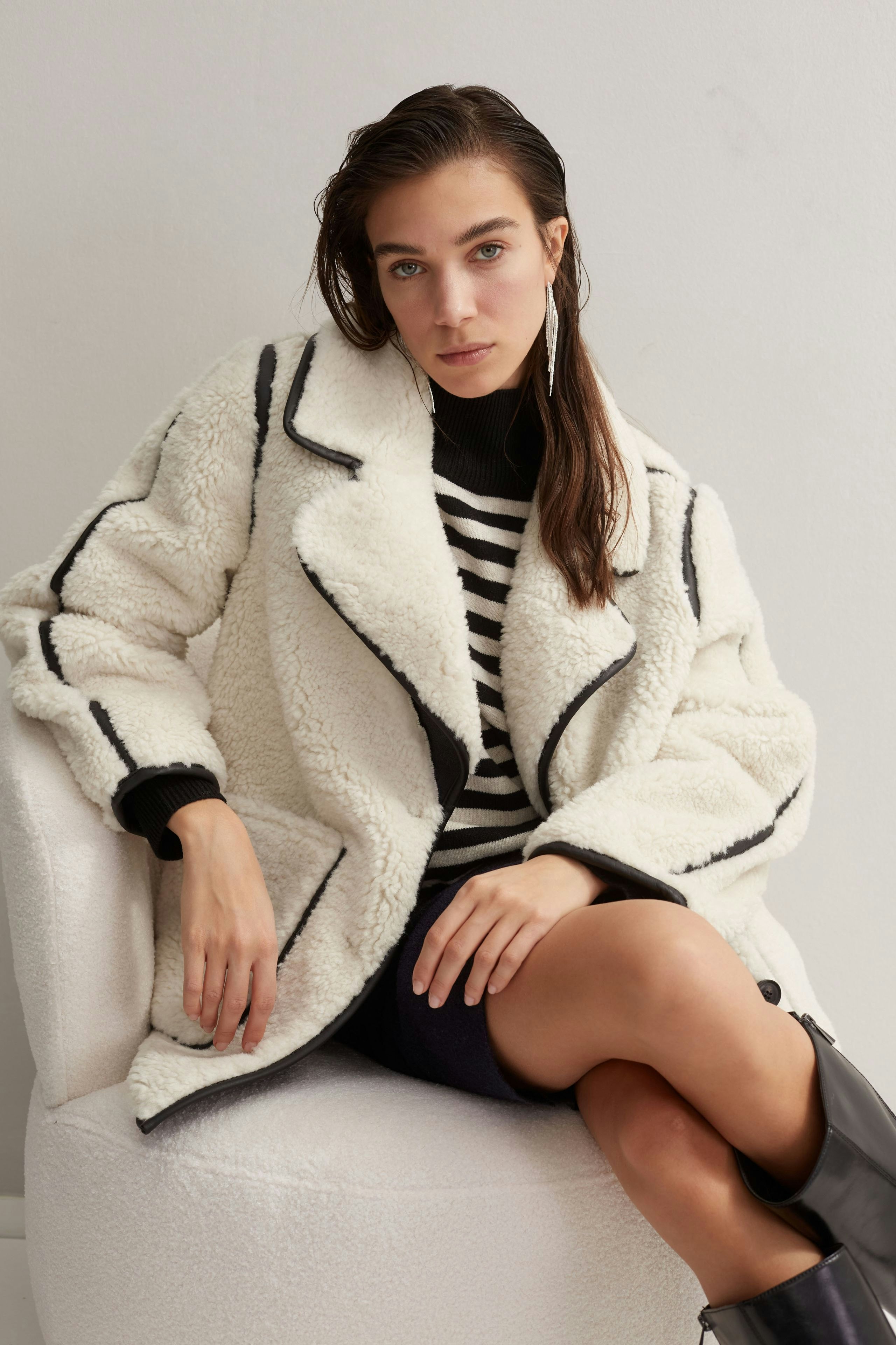 Moderne Outdoorjacke: Junge Frau in einer weißen, kuscheligen Jacke mit schwarzem Kragen sitzt entspannt.