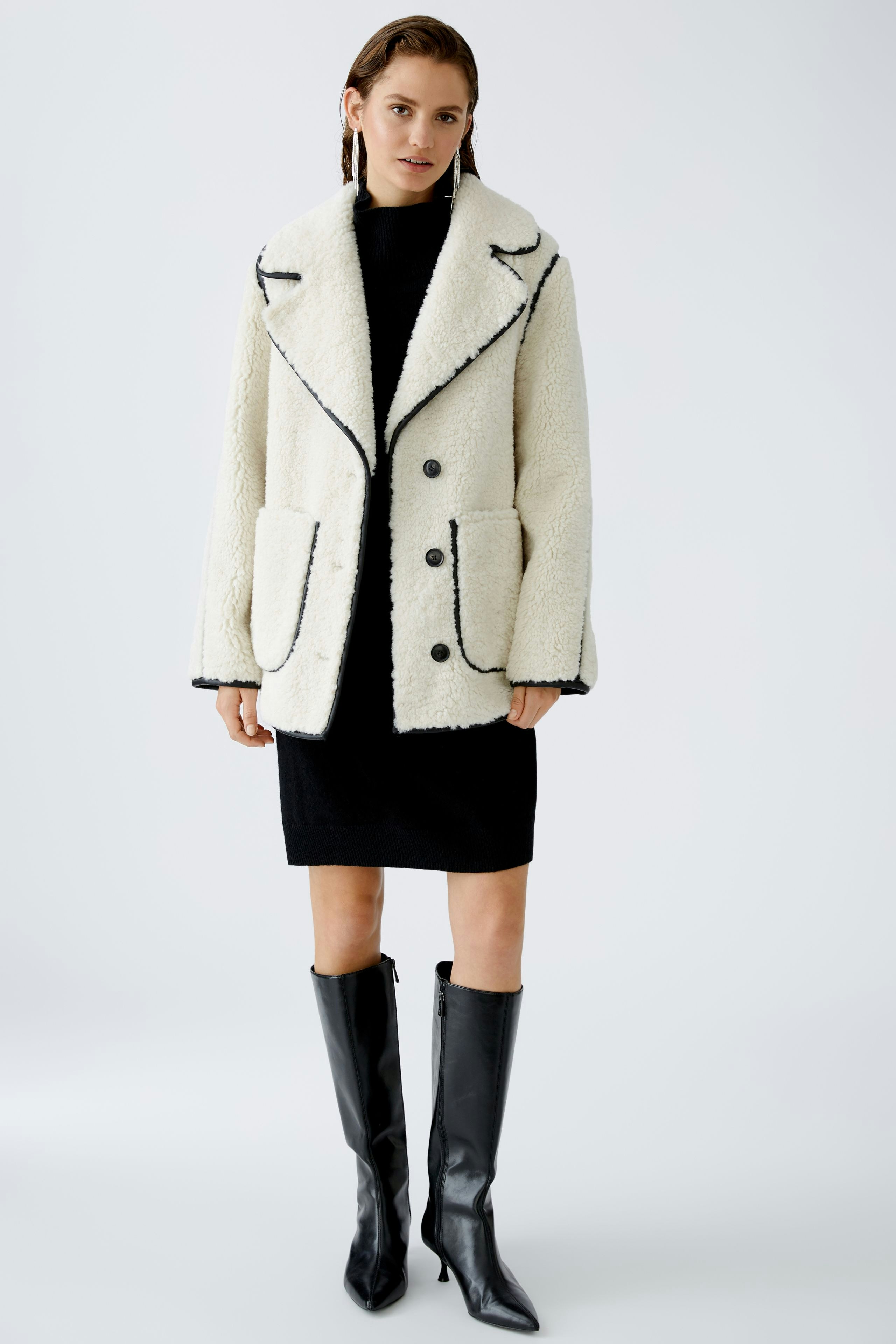 Gemütliche Outdoorjacke: Frau in einer weißen, flauschigen Jacke mit großen Taschen und elegantem Schnitt.