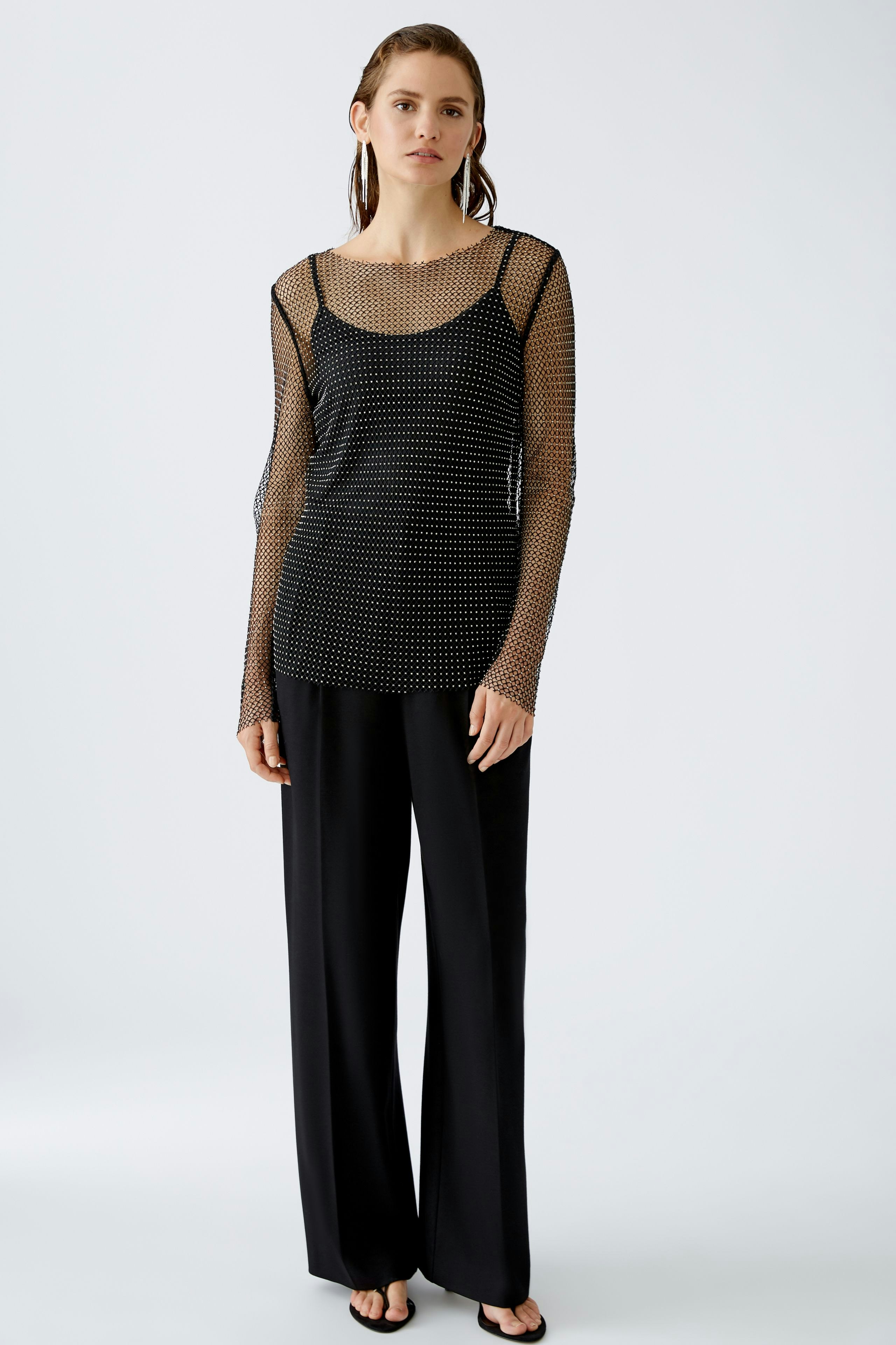 Elegantes Langarmshirt: Frau in schwarzem, transparentem Shirt mit Punkten und lässiger Hose.