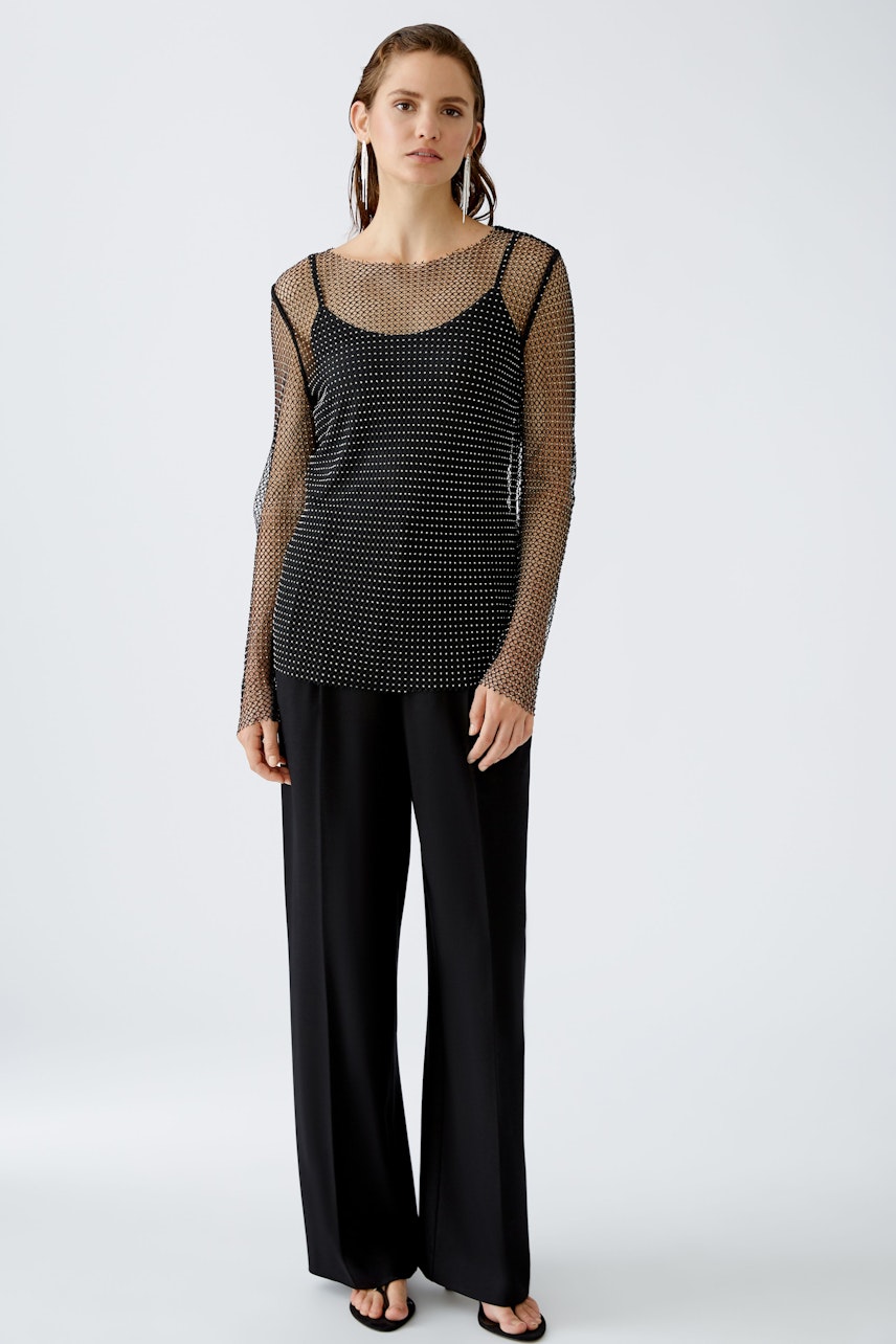 Chic long-sleeve shirt: Woman in a stylish black mesh pullover layered over a sleek top.