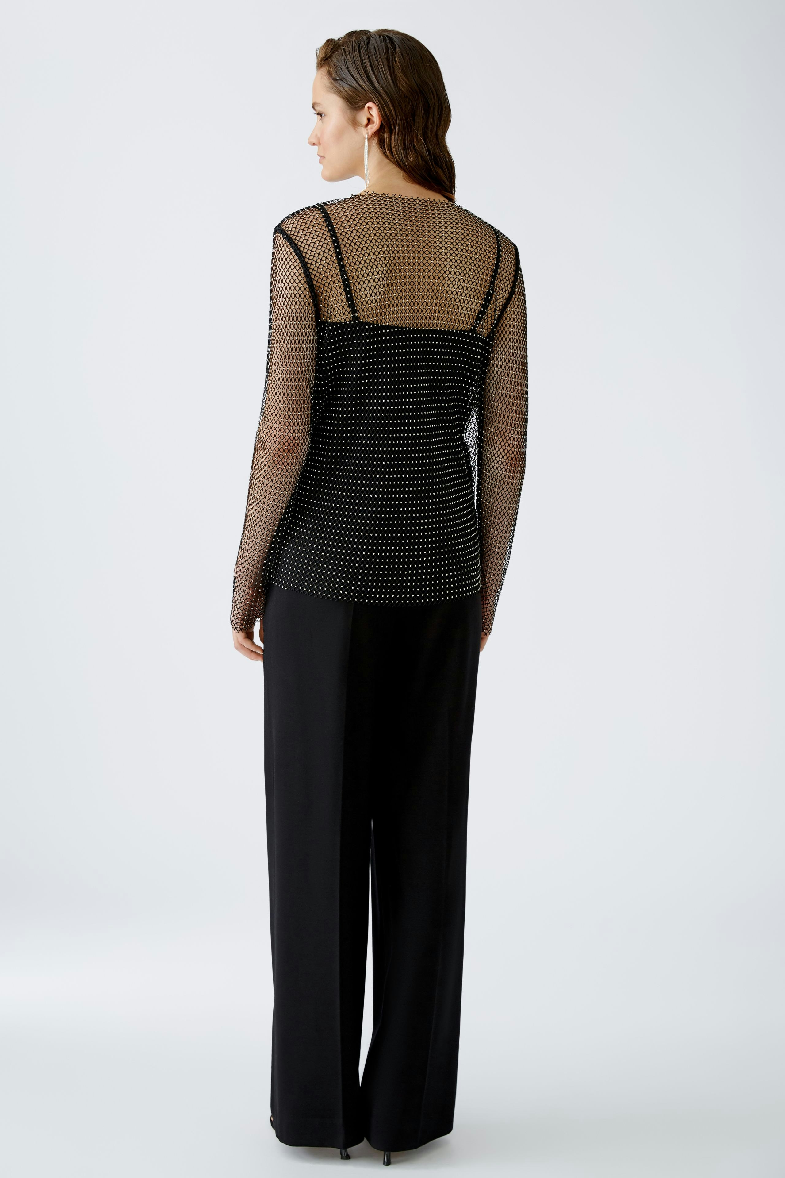 Elegantes Langarmshirt: Frau in transparentem, gepunktetem Shirt mit lässiger Hose von hinten.