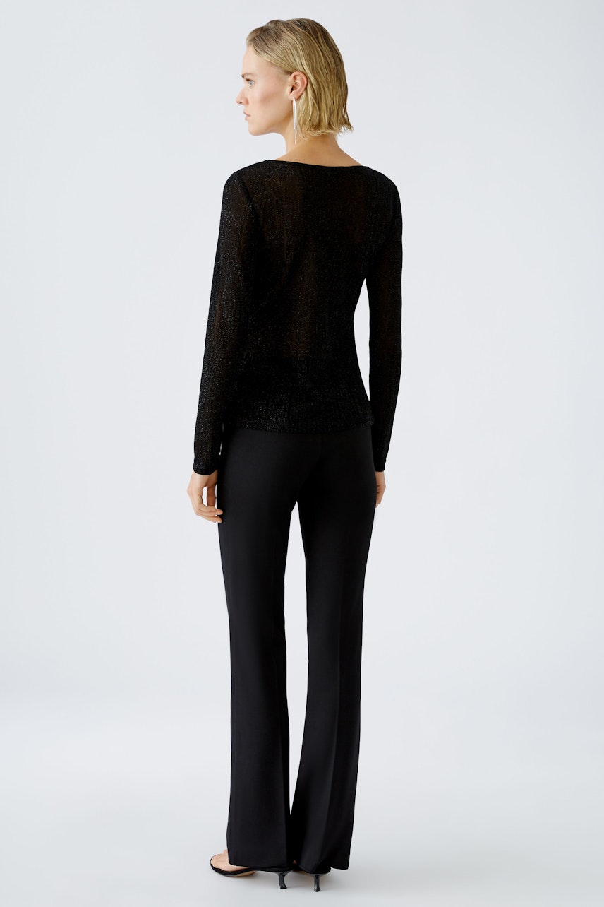 Chic long-sleeve shirt: Woman in a black, shimmering pullover paired with sleek trousers.