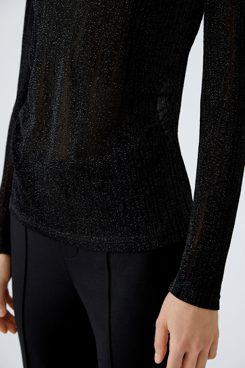 Elegant long-sleeve shirt: Woman in a black, shimmering top with a fitted silhouette.