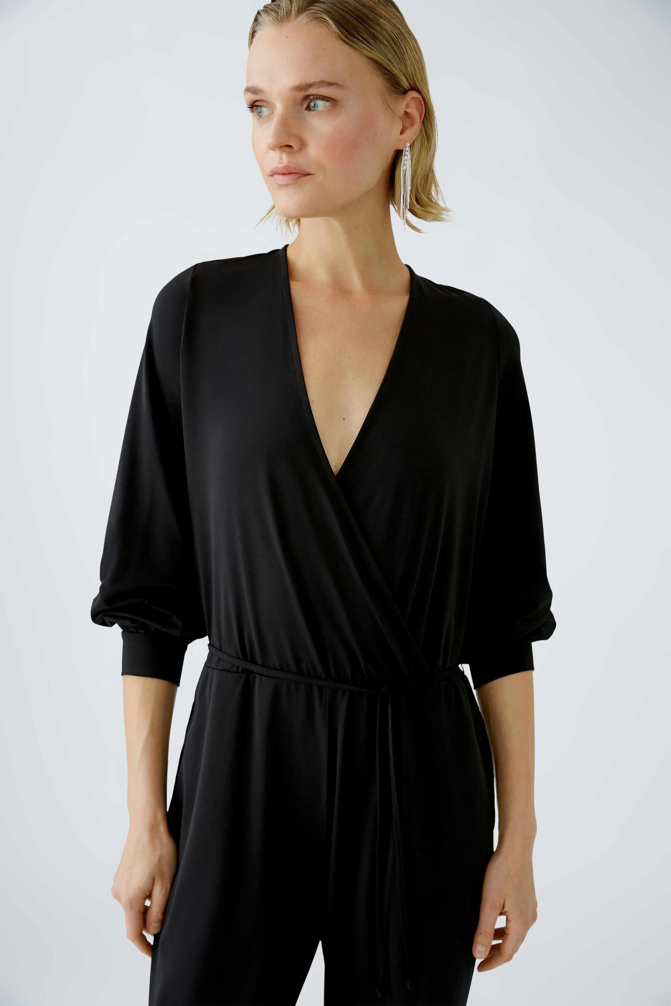 Elegant black jumpsuit: A woman in a stylish black jumpsuit with a deep V-neck and relaxed sleeves.