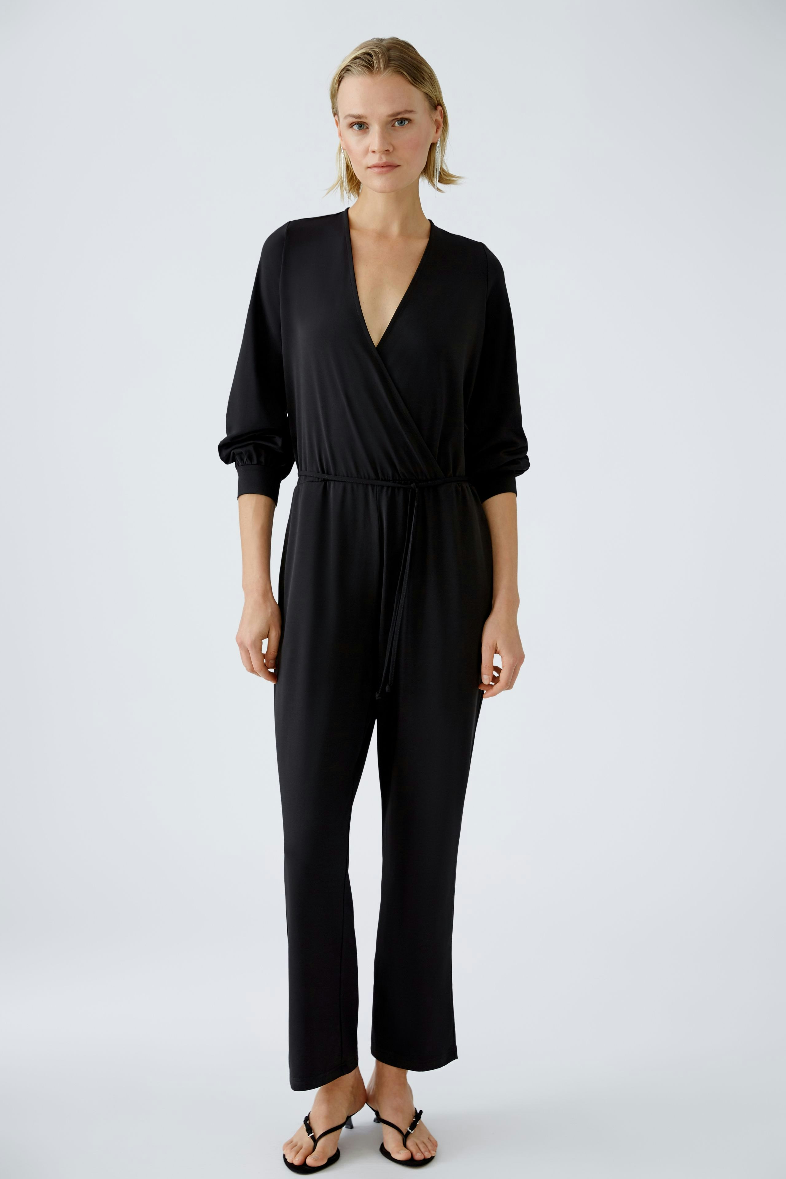 Elegant black jumpsuit: A woman in a stylish black jumpsuit with a wrap design and relaxed fit.