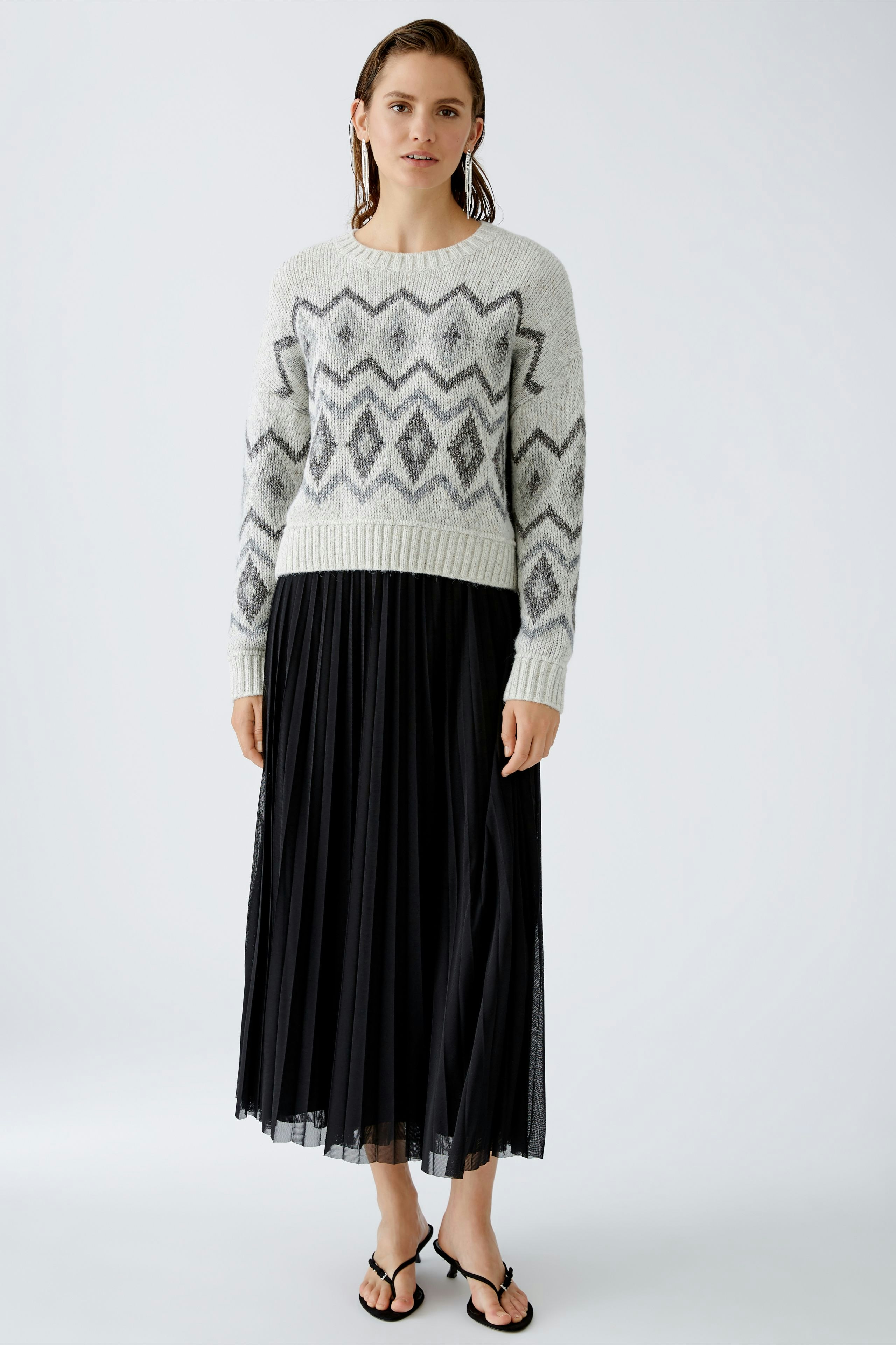 Damen-Pullover: Frau in grauem Strickpullover mit geometrischem Muster und schwarzem, fließendem Rock.