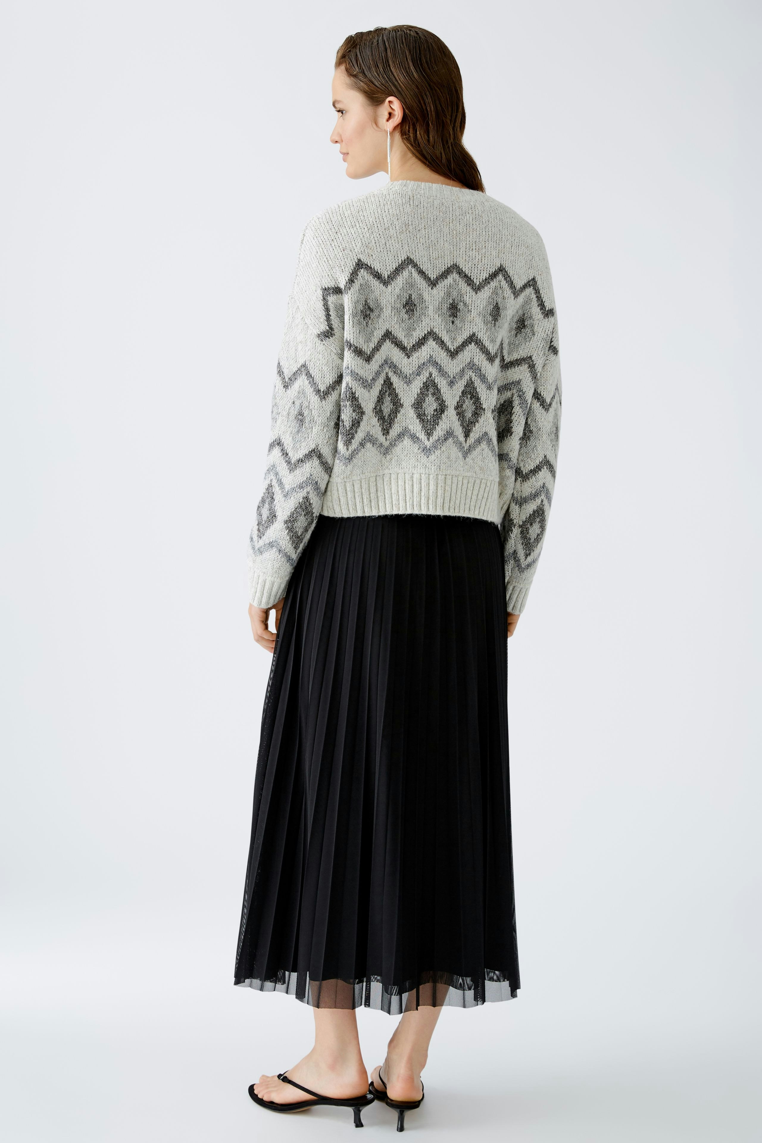 Damen-Pullover: Frau in grauem Strickpullover mit geometrischem Muster und schwarzem, plissiertem Rock.