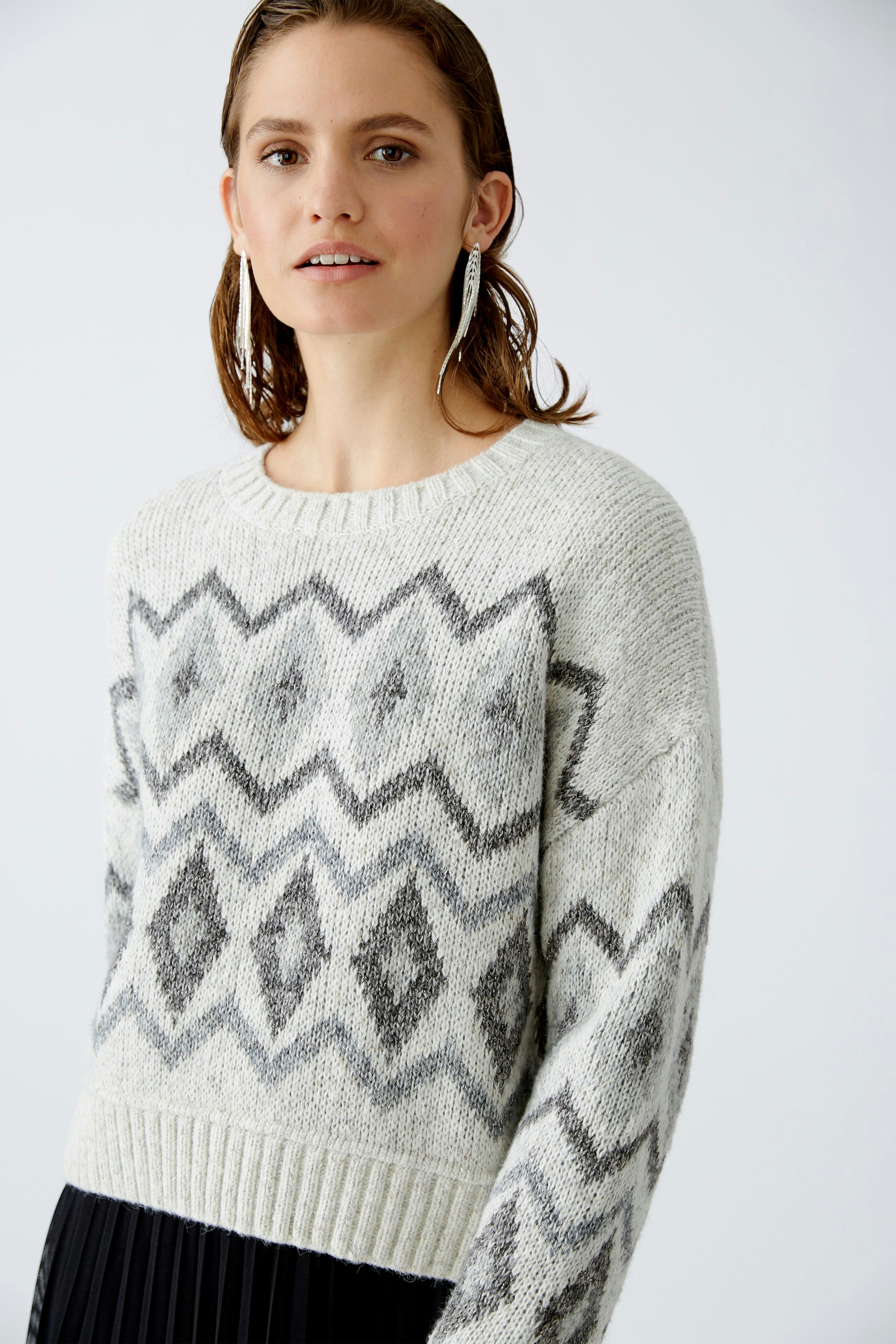 Damen-Pullover: Frau trägt einen grauen Pullover mit geometrischem Muster und lässigem Schnitt.