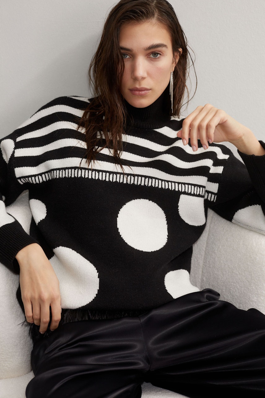 Modern pullover: Woman in a black and white striped pullover with polka dots, exuding confidence.