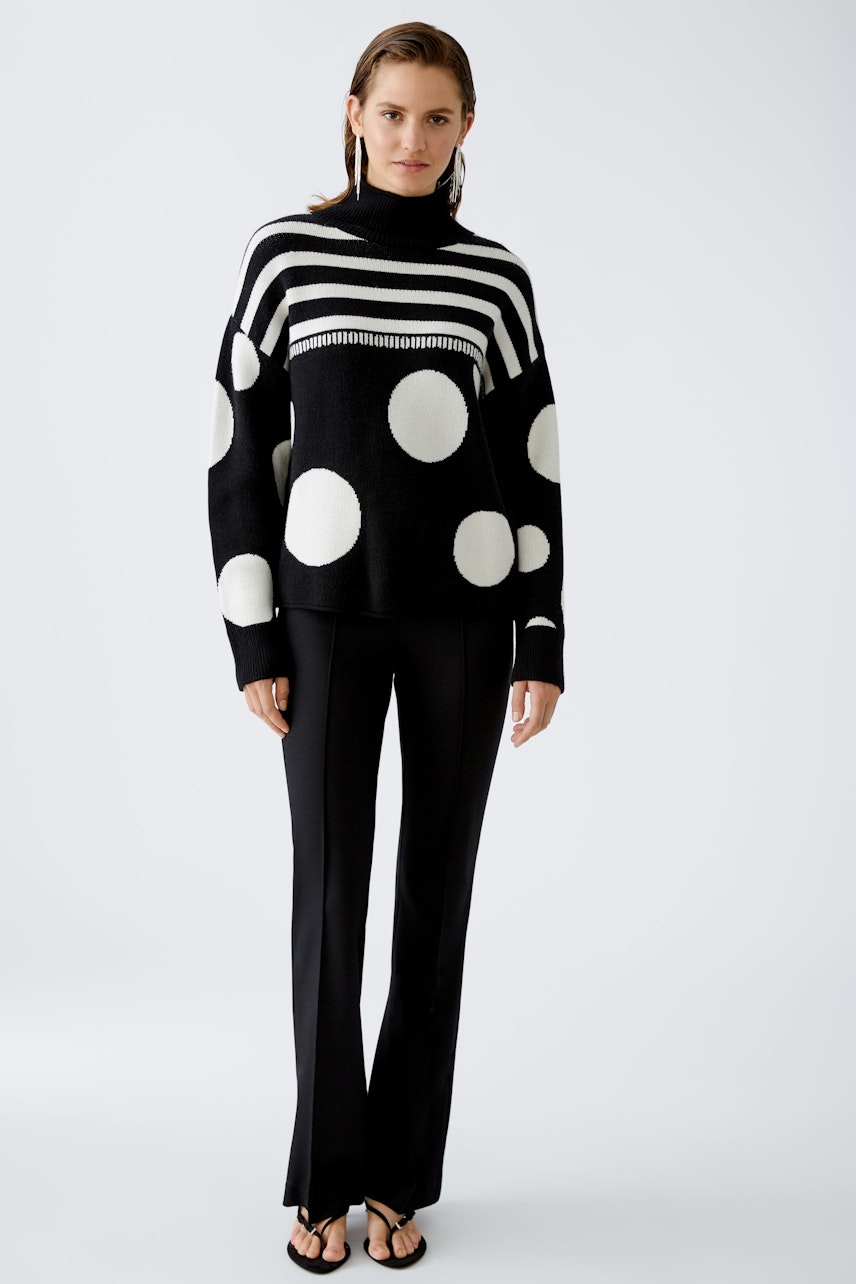 Modern women's pullover: A woman in a black and white striped pullover with polka dots stands confidently.