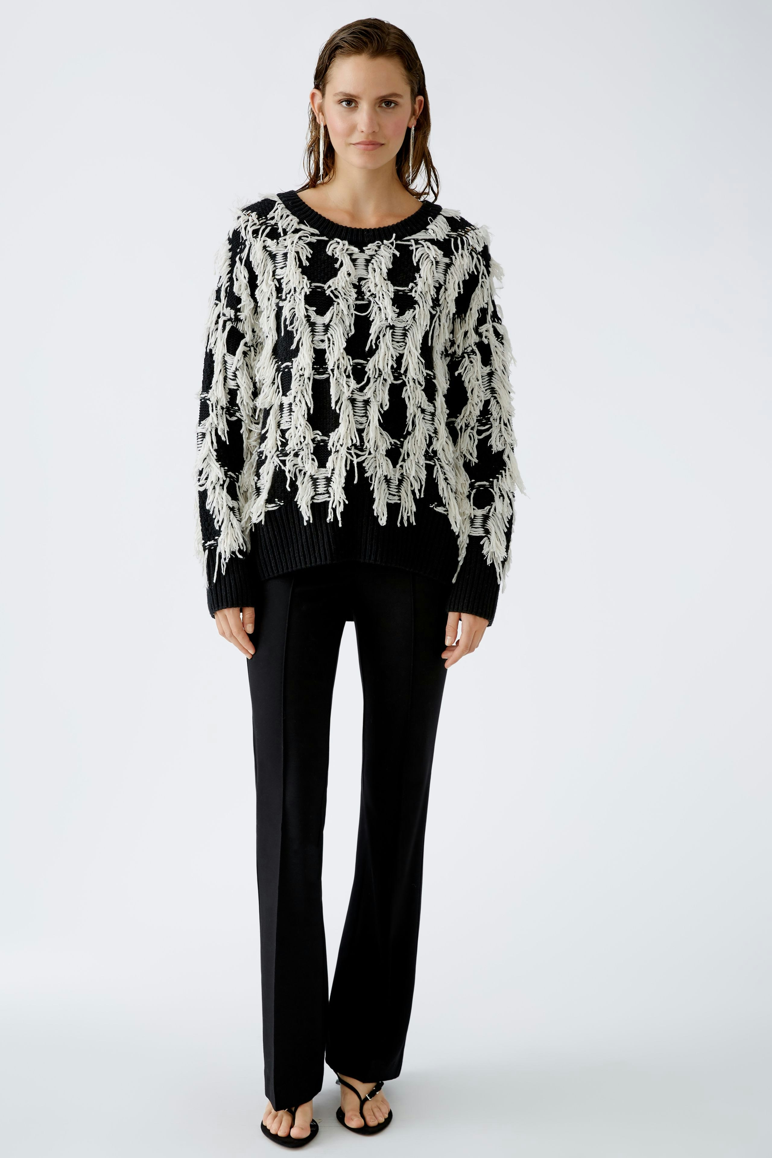 Modern pullover: Woman in a black and white fringed pullover paired with sleek black pants.