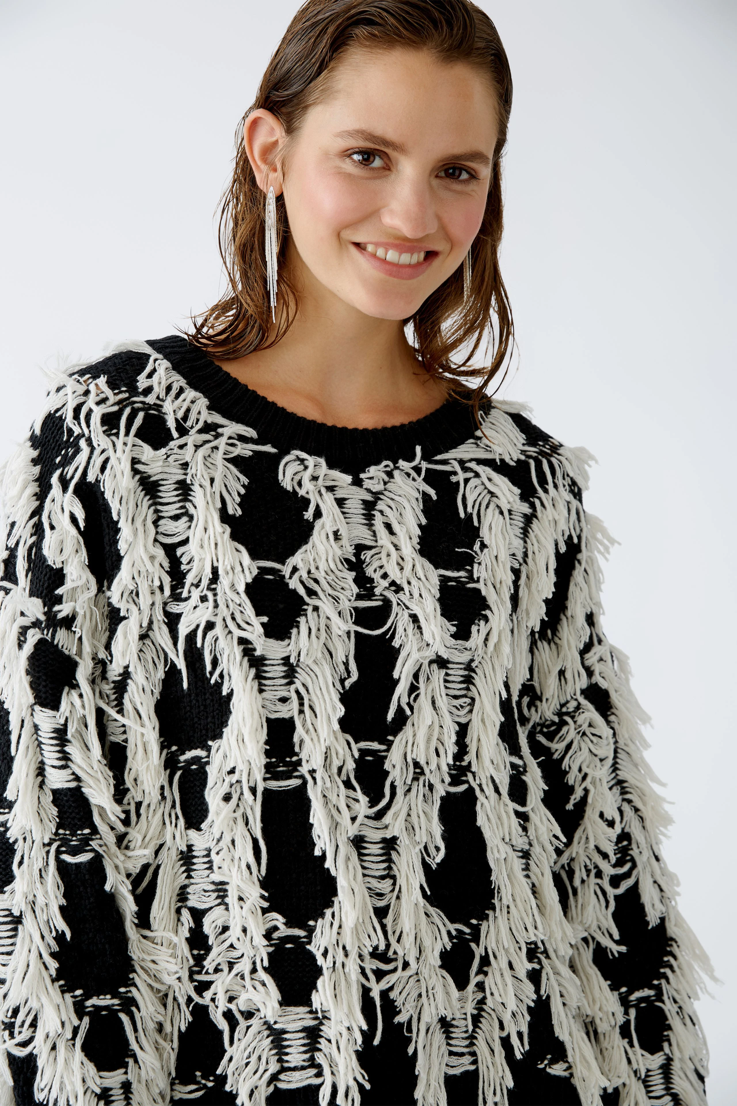 Modern pullover: Woman in a black and white fringed pullover smiles confidently.