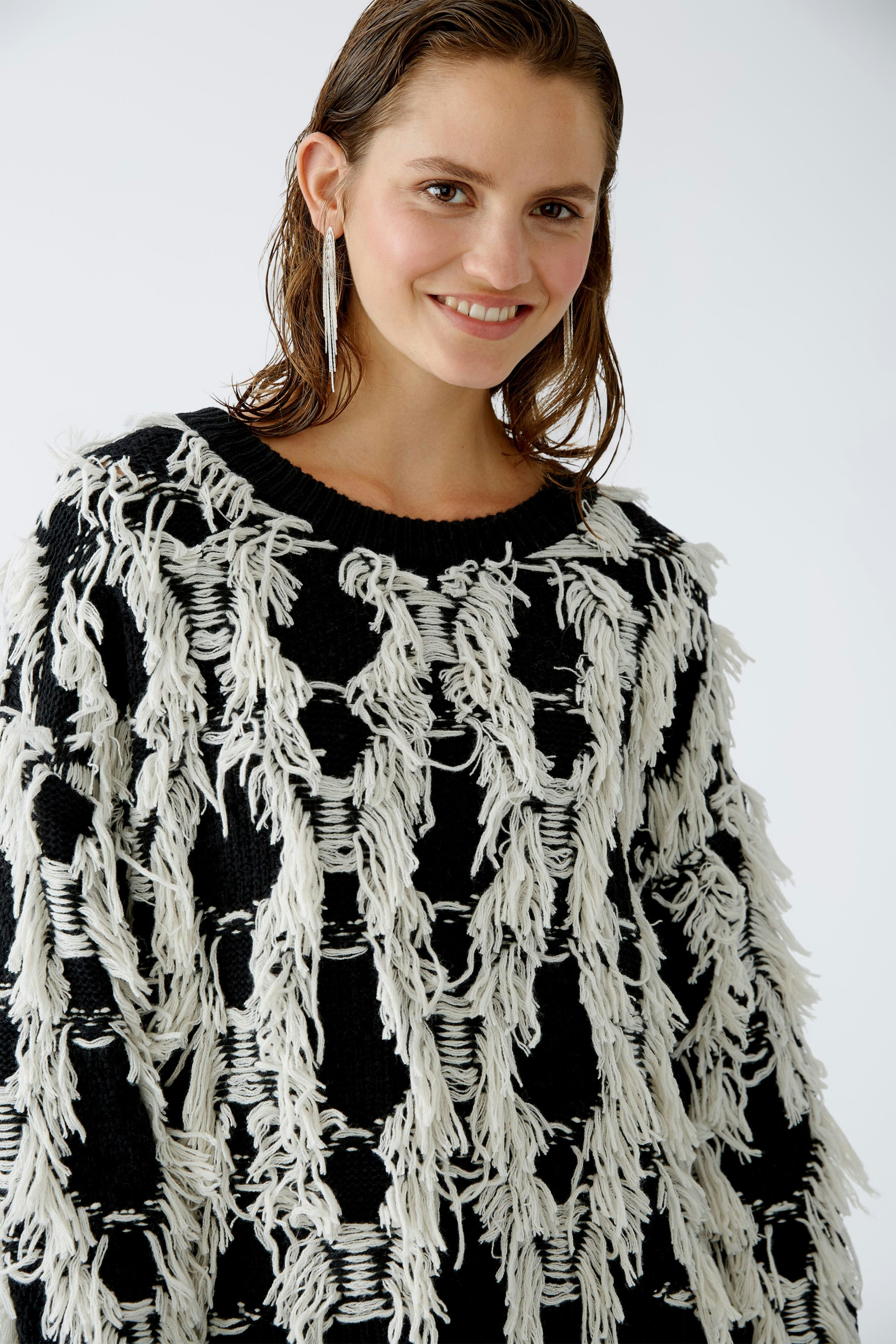 Modern pullover: Woman in a black and white fringed pullover smiles confidently.