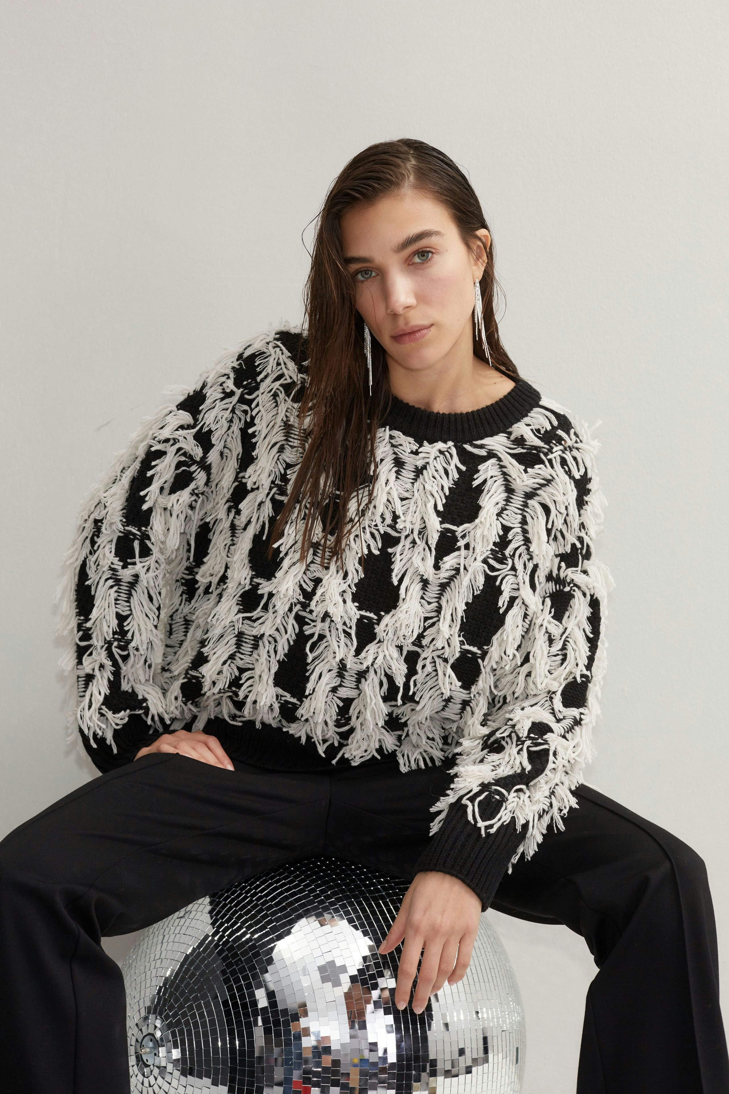 Modern pullover: Young woman in a black and white fringed pullover poses confidently on a disco ball.