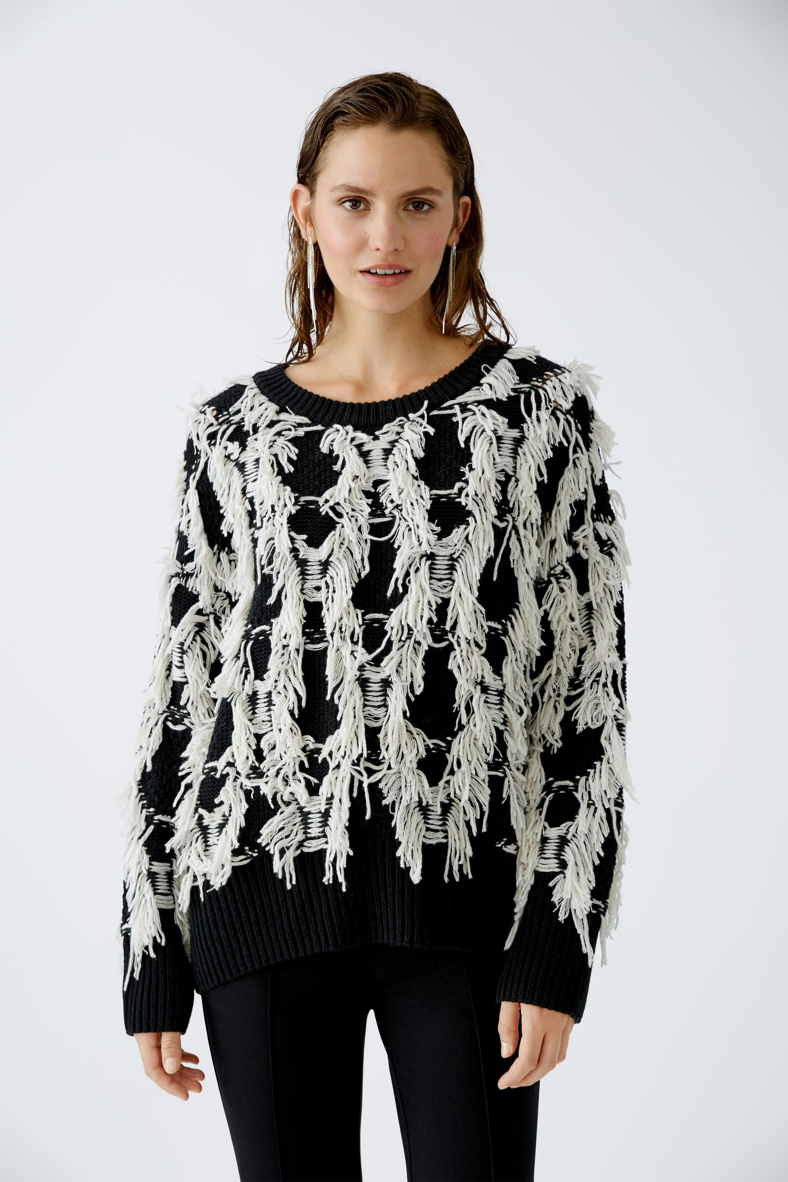 Modern women's pullover: A woman in a black pullover with white fringes poses confidently.